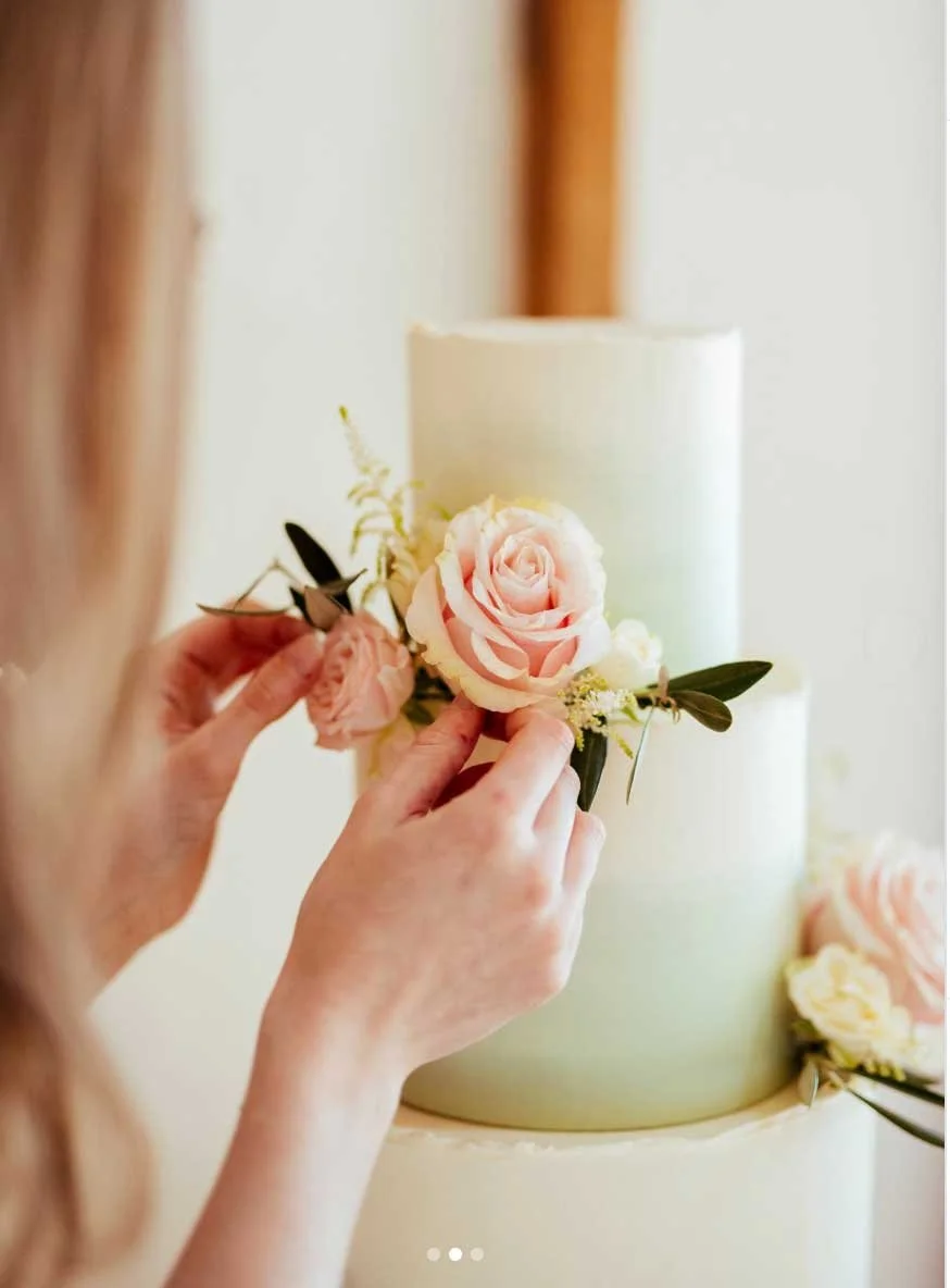 Person decorating a wedding or celebration cake with pink and white roses.