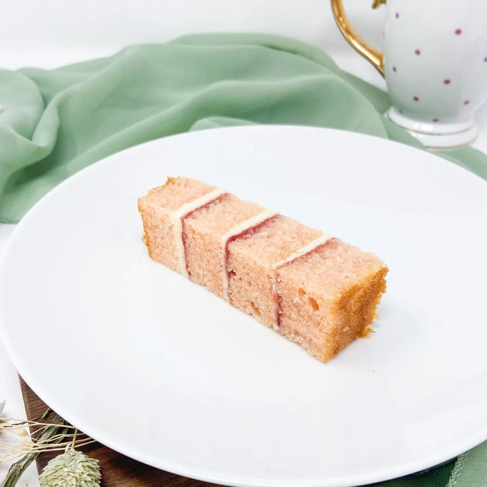 A slice of pink sponge cake with white frosting on a white plate.