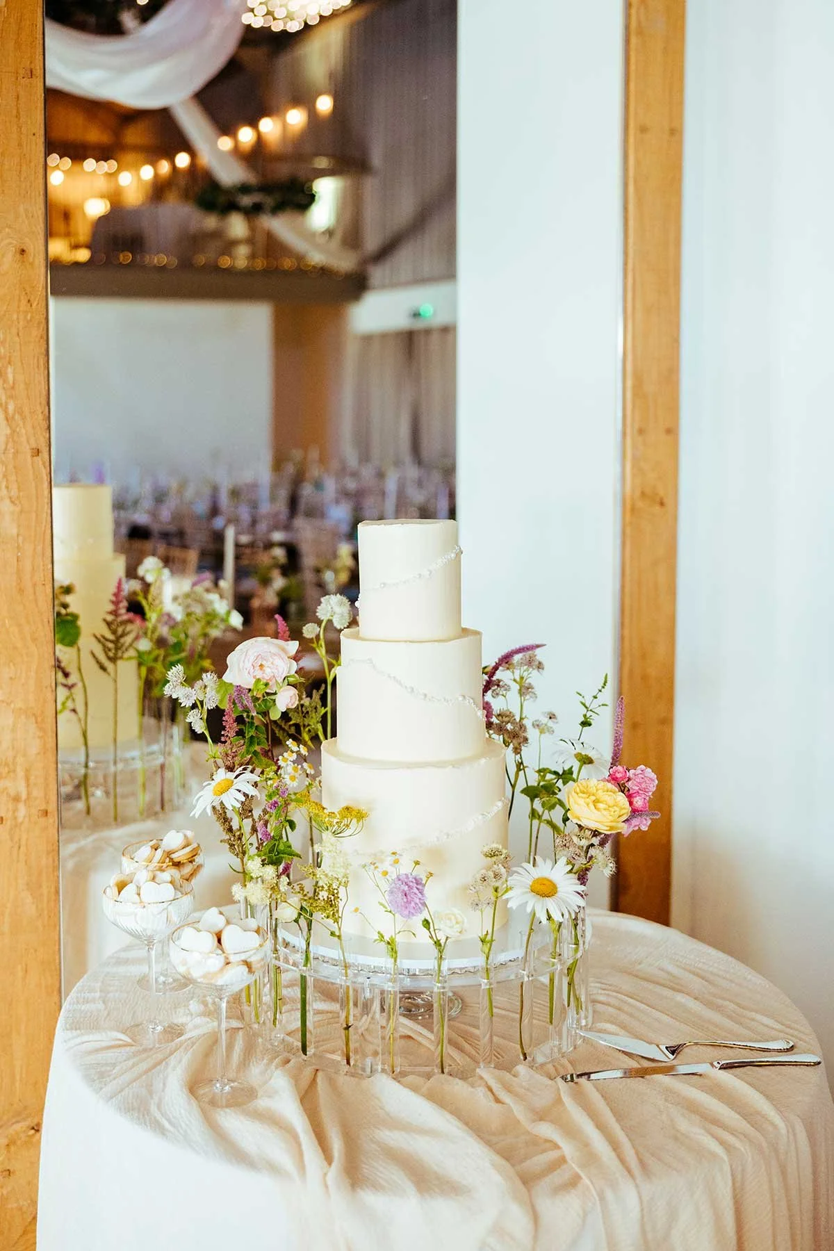 A white wedding cake on a table decorated with flowers and candy.