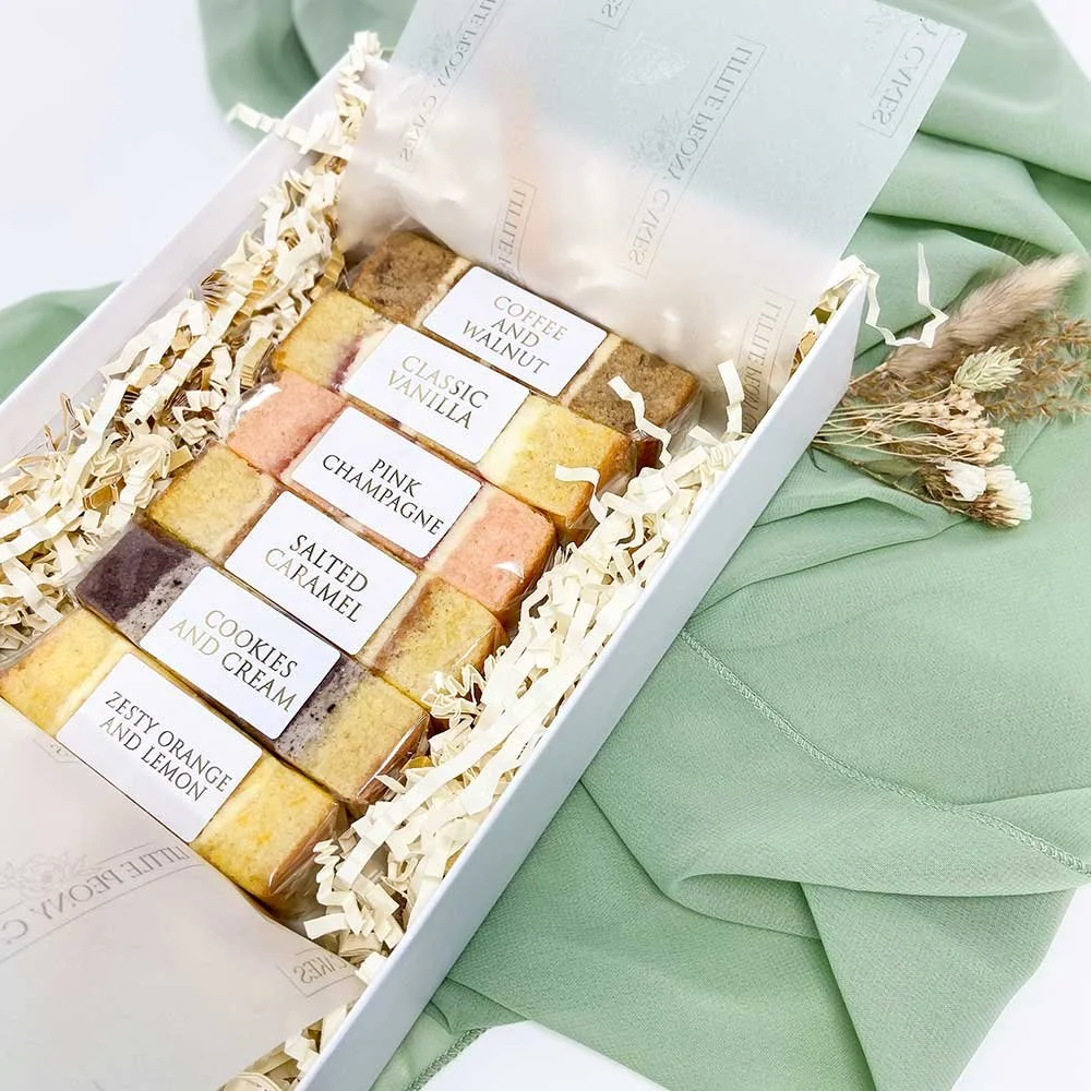 A box of assorted flavored bath bombs labeled with different names such as coffee and walnut, classic vanilla, pink champagne, salted caramel, cookies and cream, and zesty orange and lemon, arranged on shredded paper inside the box.