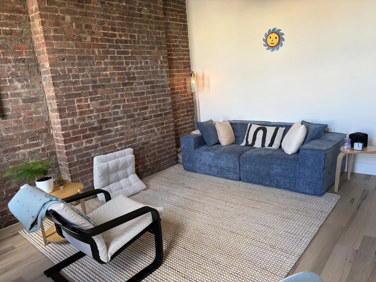The Brooklyn North therapy room in Greenpoint, Brooklyn, with a blue sofa, an exposed brick wall and a reading chair