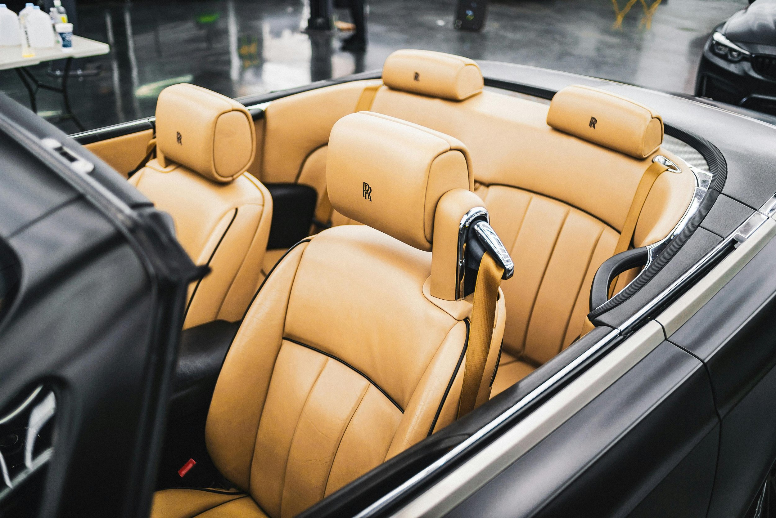 Interior of a luxury convertible car with tan leather seats, featuring seat headrests embroidered with the 'RR' logo, parked on a rainy day.