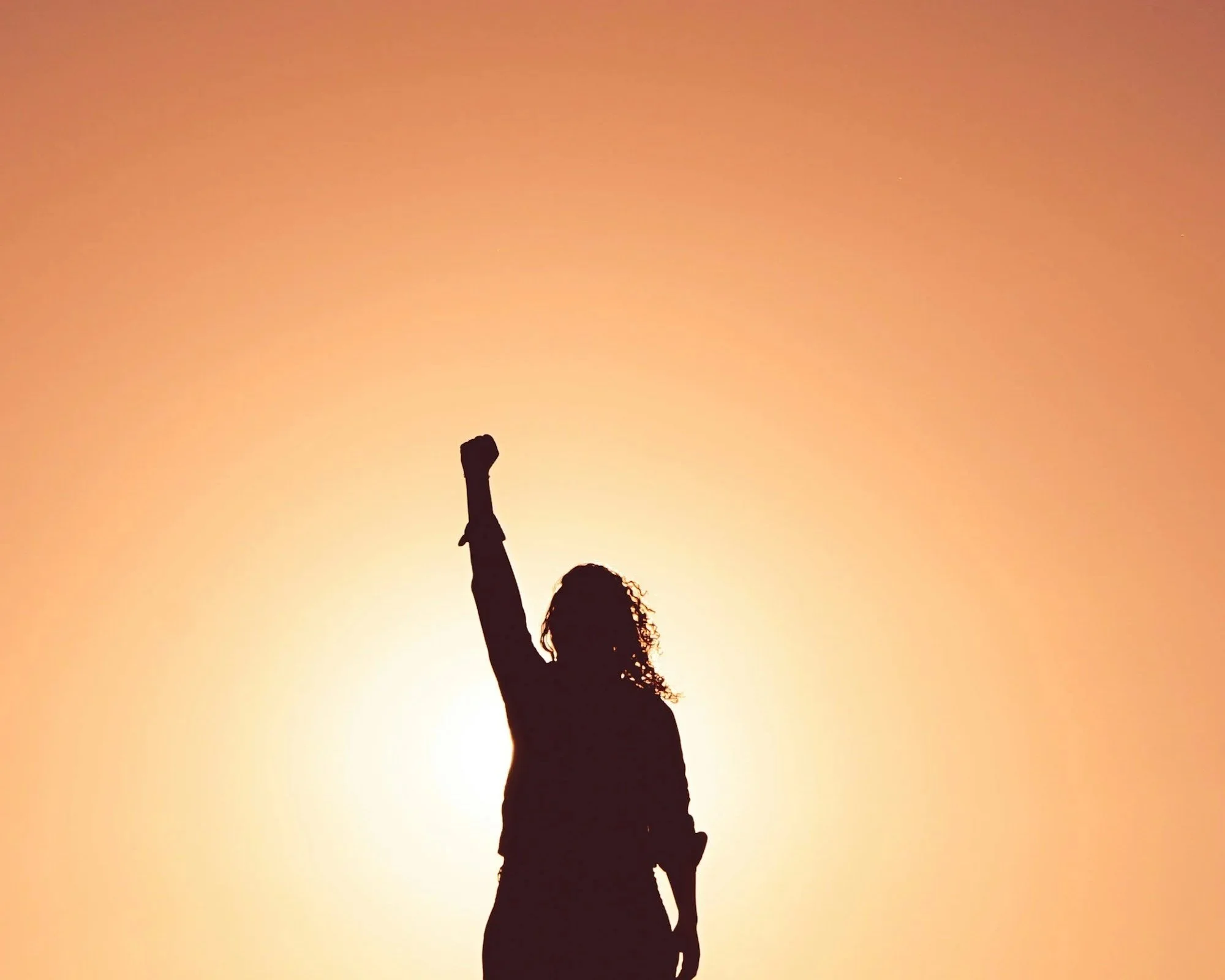 Silhouette of a woman standing with one arm raised against a sunset background