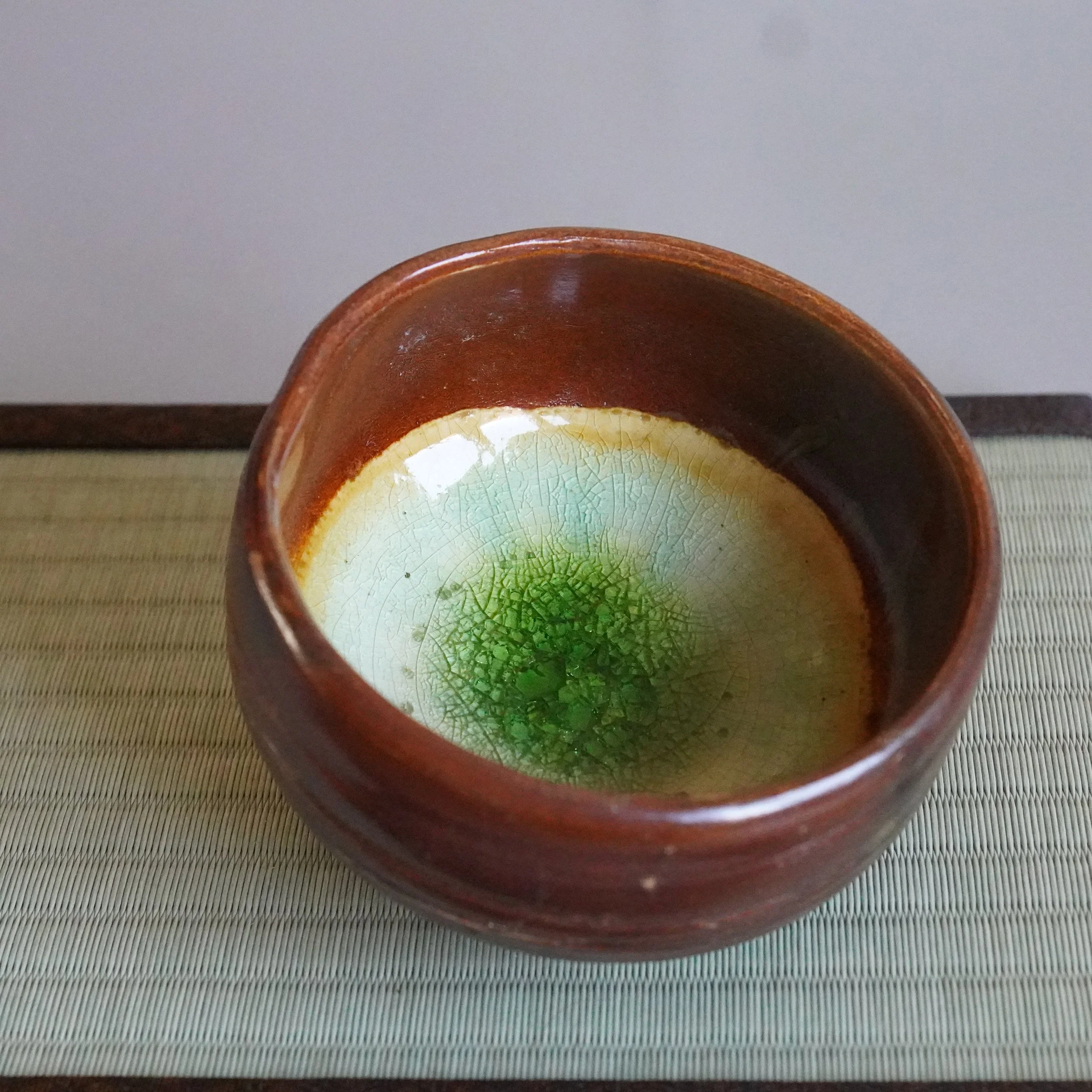 Close-up of the rim of a ceramic mug with a textured interior showing a gradient from cream to bright green, placed on a textured fabric surface.