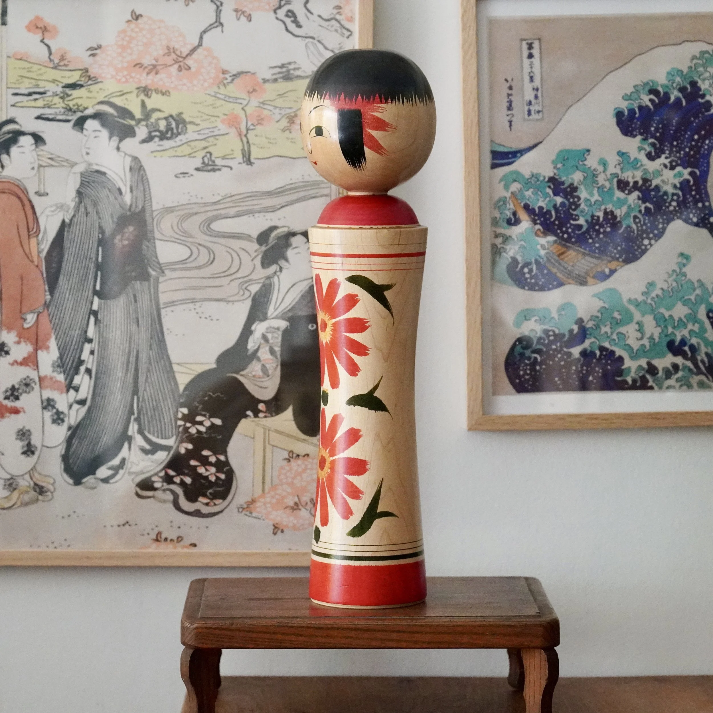 Tall Ginzan kokeshi doll by Izu Mamoru, light wood body painted with red chrysanthemums and green leaves. Features a black bob, minimalist face, and red collar and base.