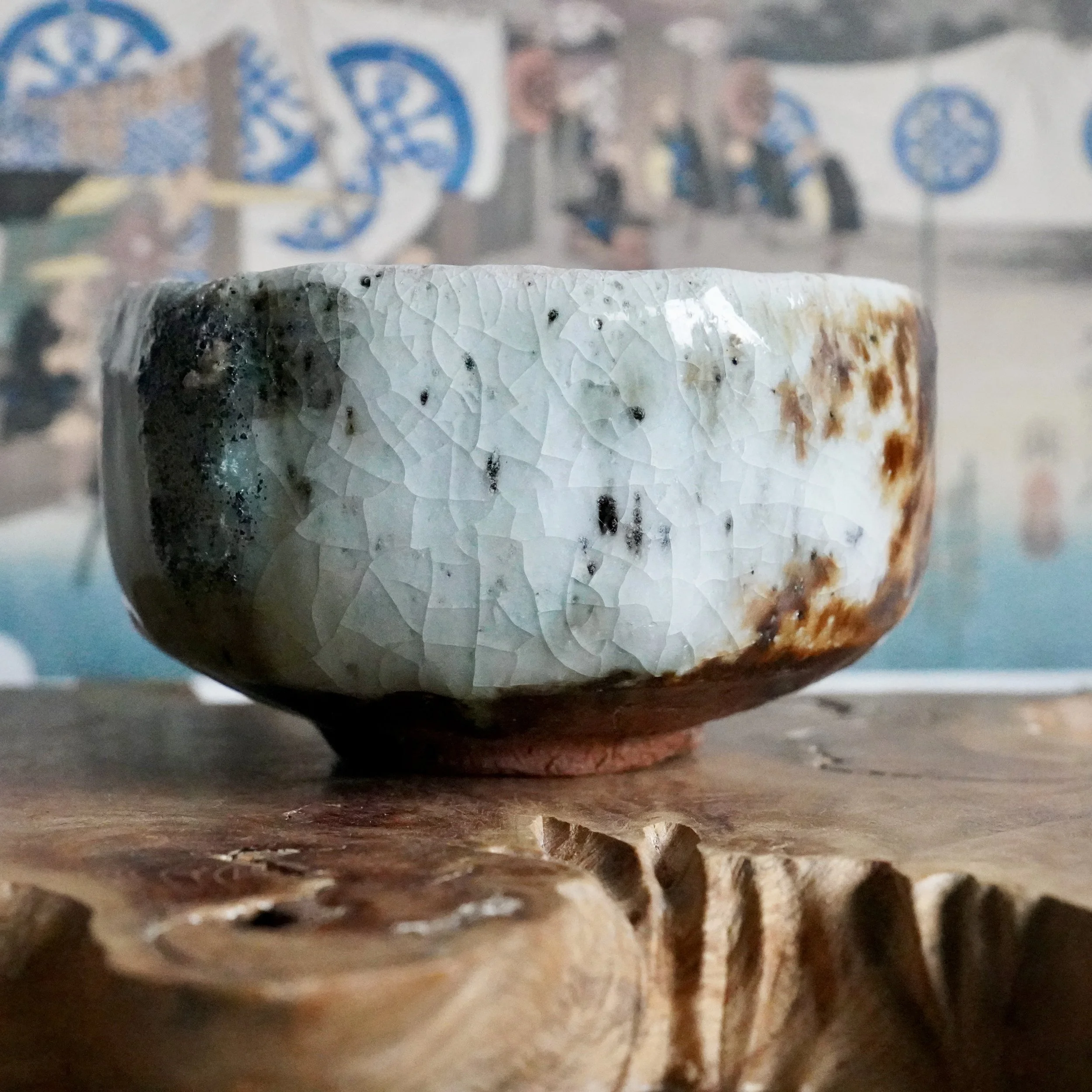 Deguchi Eiji chawan with crackled pale glaze, deep green, and rust-brown, on a wooden surface.