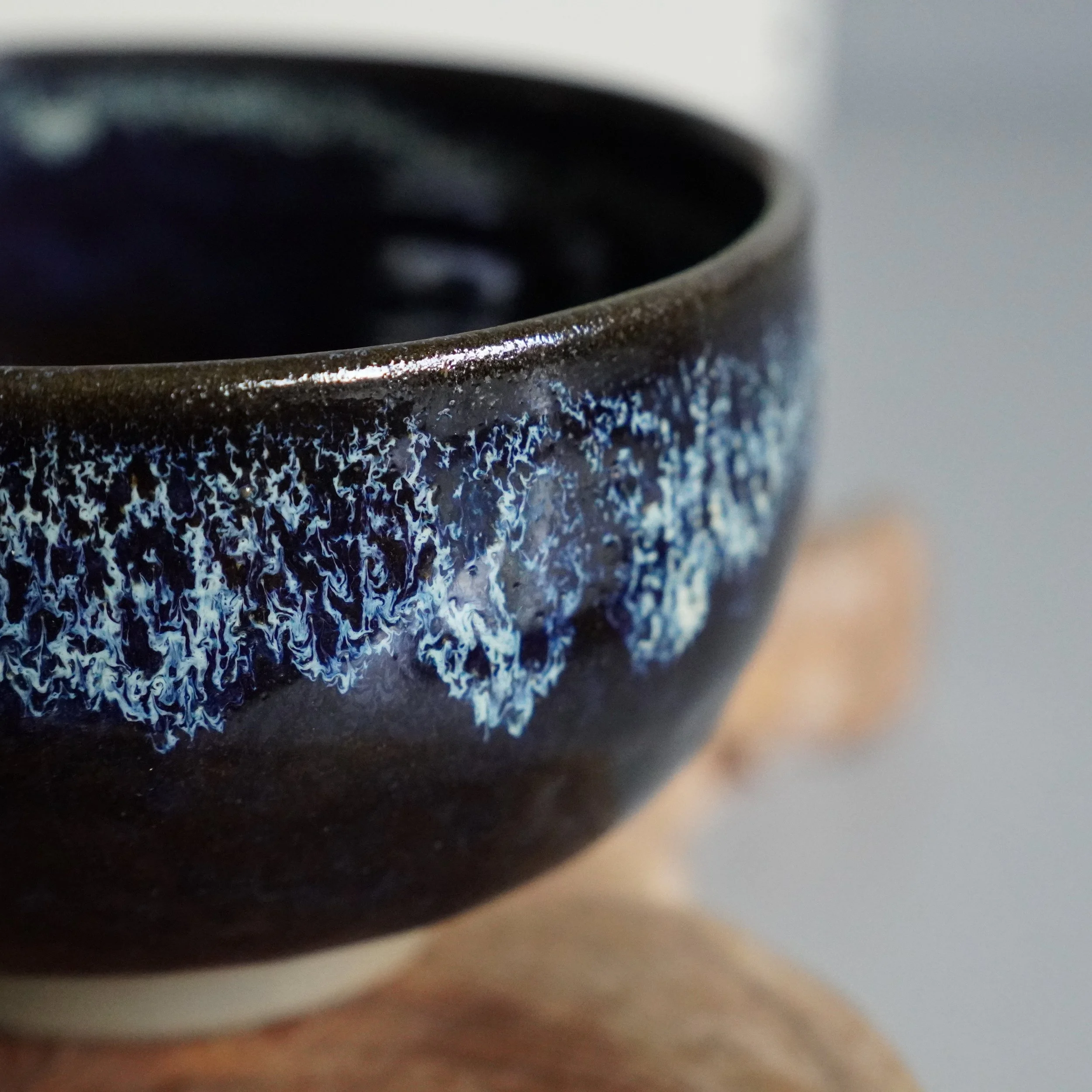 Close-up of a dark brown ceramic matcha bowl by Rokuhō, with mottled blue glaze over its upper body and rim.