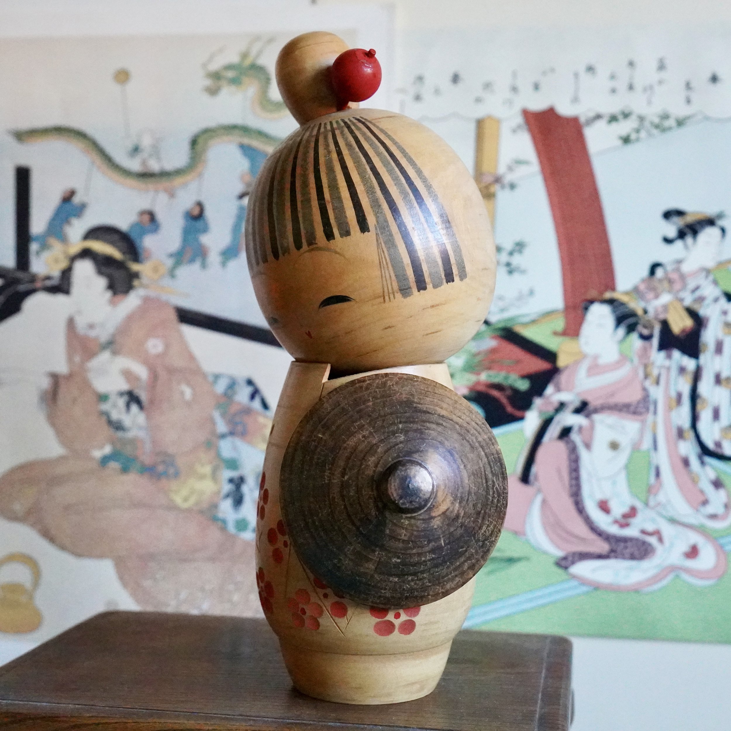 Three quarter back view of Sato Suigai sōsaku kokeshi with carved plum blossom decoration