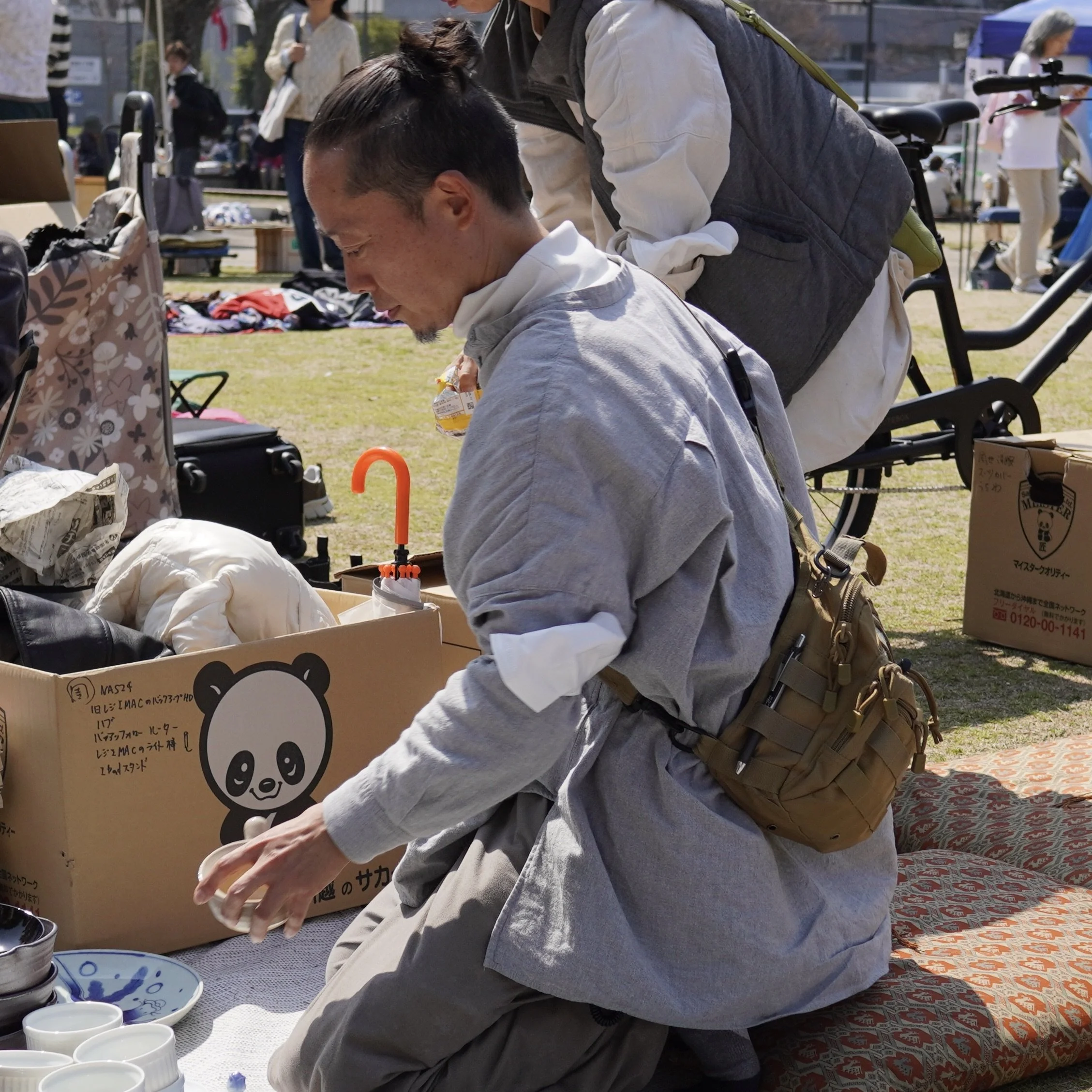 A Japanese man carefully organizes and prepares items for sale on a blanket at a local flea market, showing the authentic and slow process of finding unique vintage pieces.