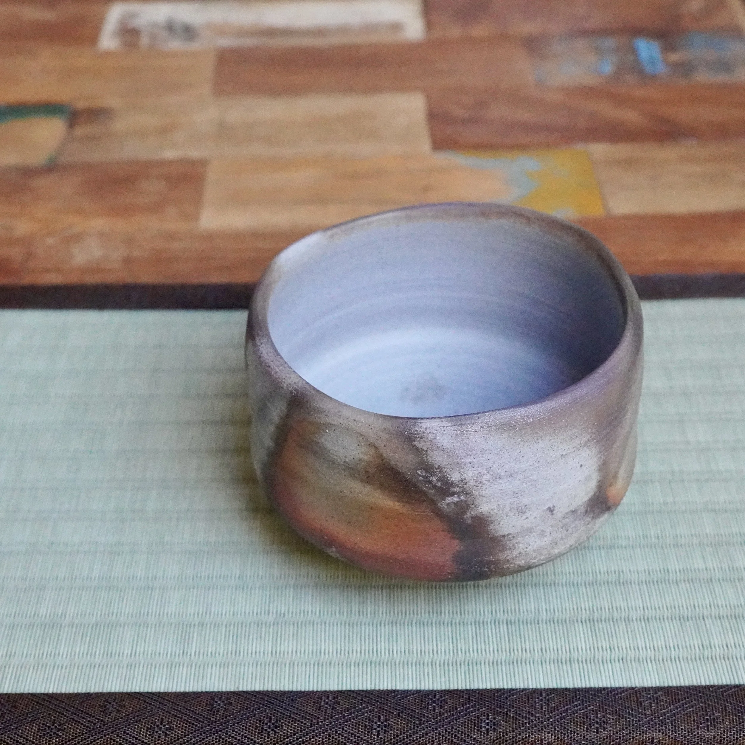 Inomata Masaaki's Sangiri Bizen chawan, featuring an exterior with rust, burnt orange, and ash grey fire marks, and a pale grey interior, on a tatami mat.