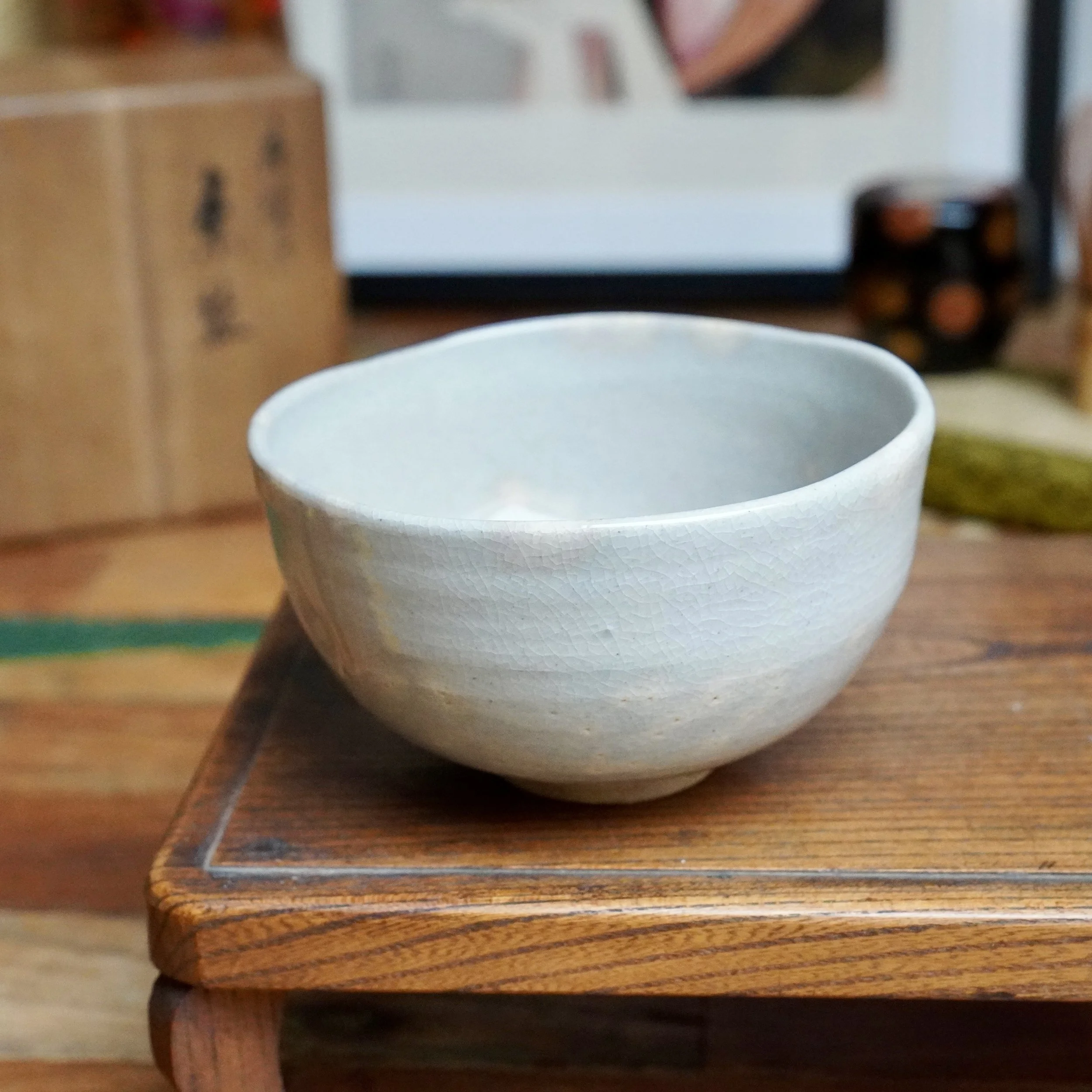 Nagasawa Minoru, Izushi-gama chawan. Grey-blue crackle-glazed tea bowl with warm pink interior, resting on a dark wood stand.