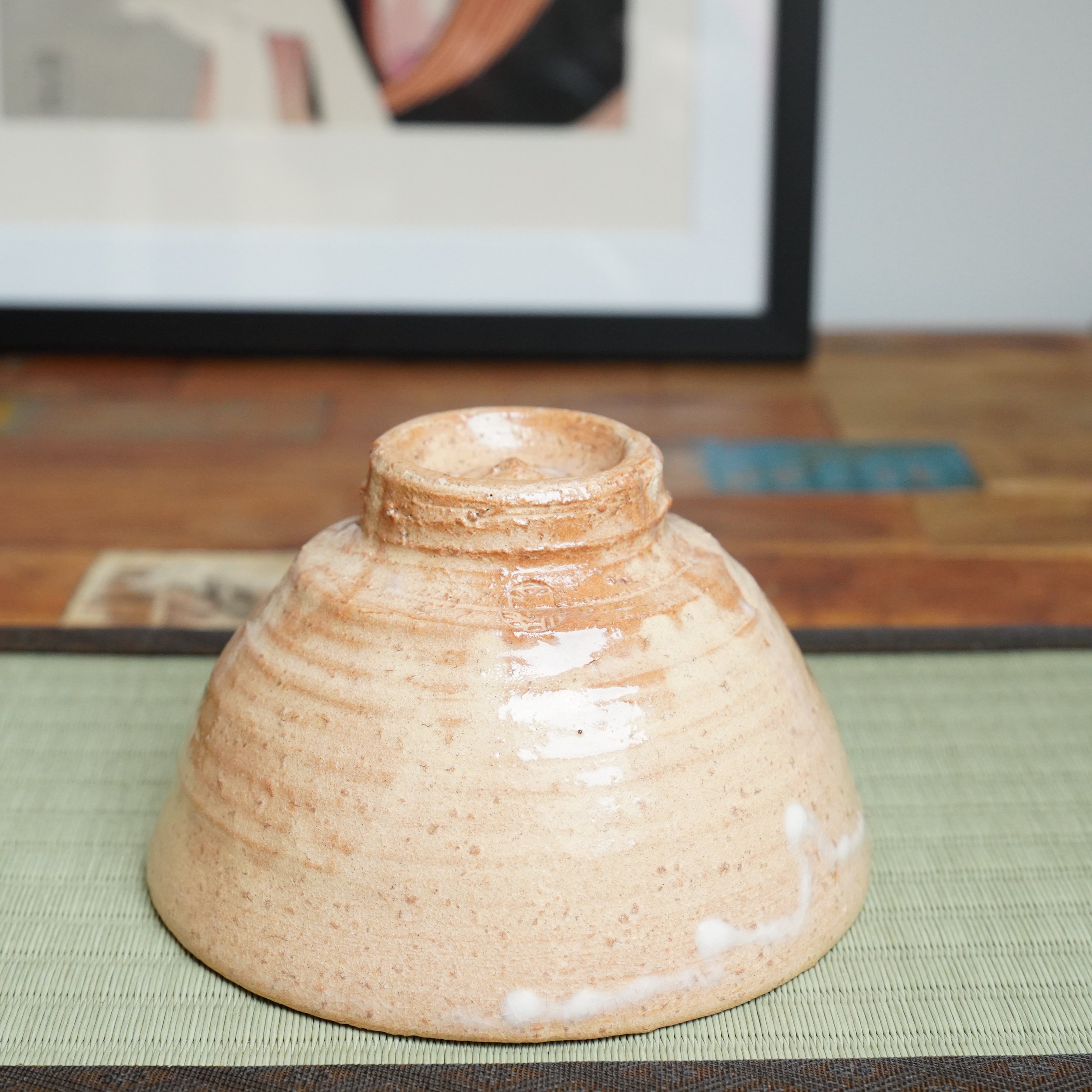 Hagi-yaki chawan by Kaneko Nobuhiko, inverted on a tatami mat. Salmon-pink body, speckled with iron, shows wheel ripples and white glaze drips on the base.