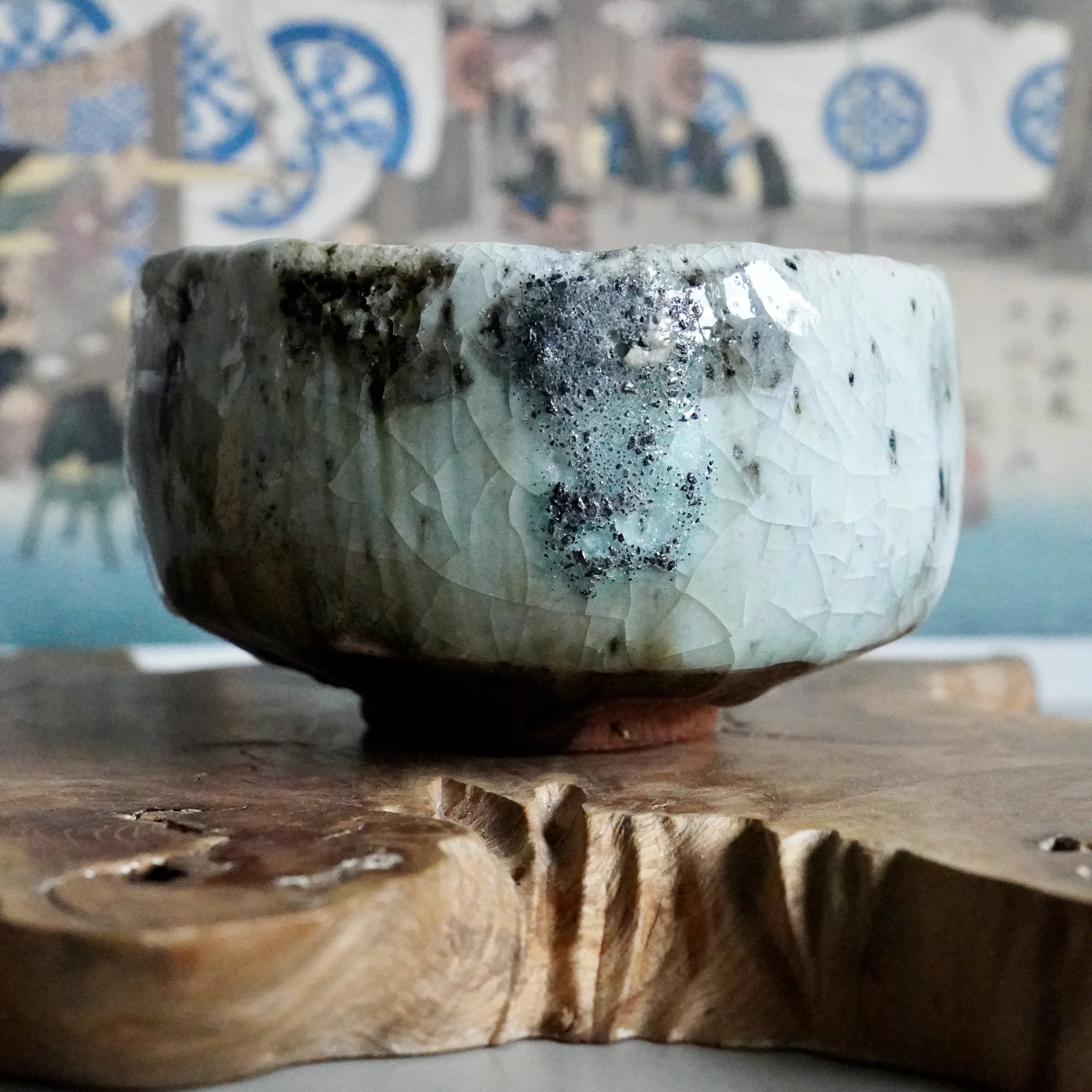 Deguchi Eiji chawan, light blue-green crackled glaze with dark speckled areas, on a rustic wood slab.