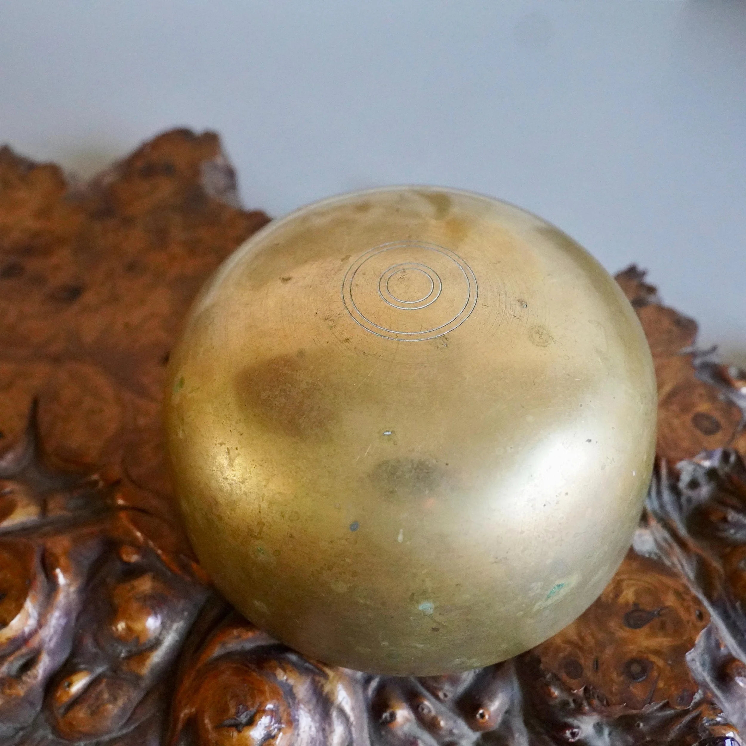 Close-up of engraved concentric ring mark on base of bronze orin bowl, wooden burl stand