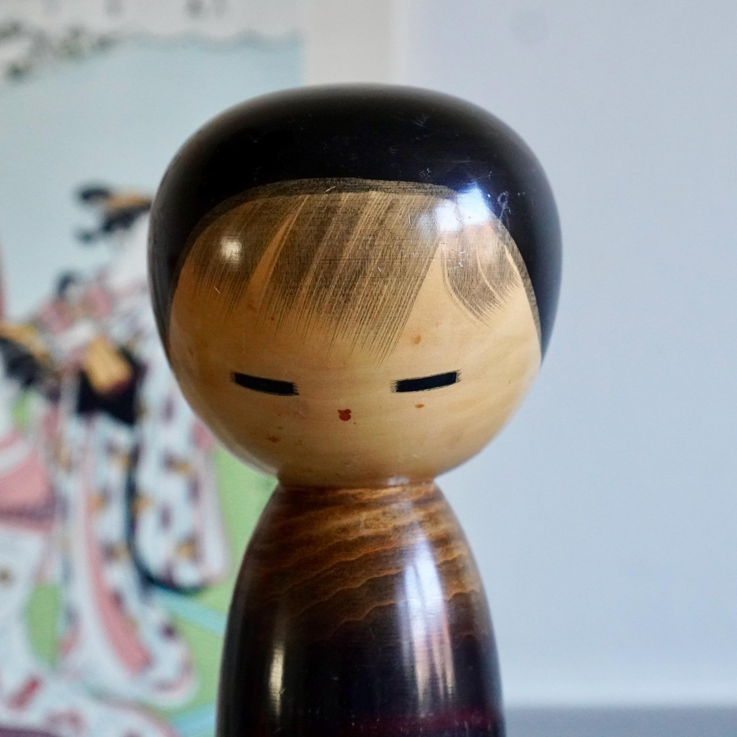 Close up of Watanabe Masao sosaku kokeshi face, closed eyes and painted features on pale wood