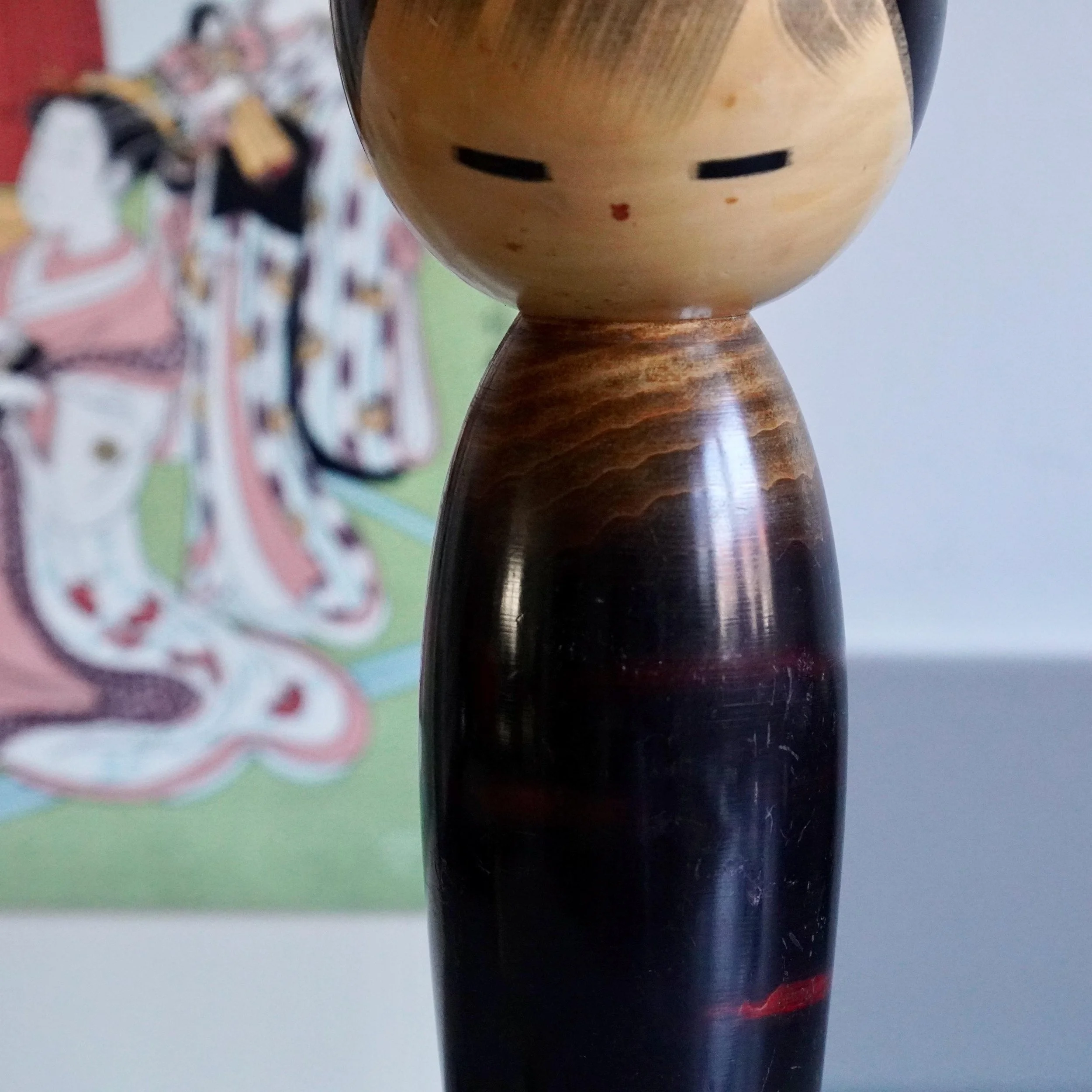 Close up angle of Watanabe Masao kokeshi head and shoulders, dark wood grain trunk