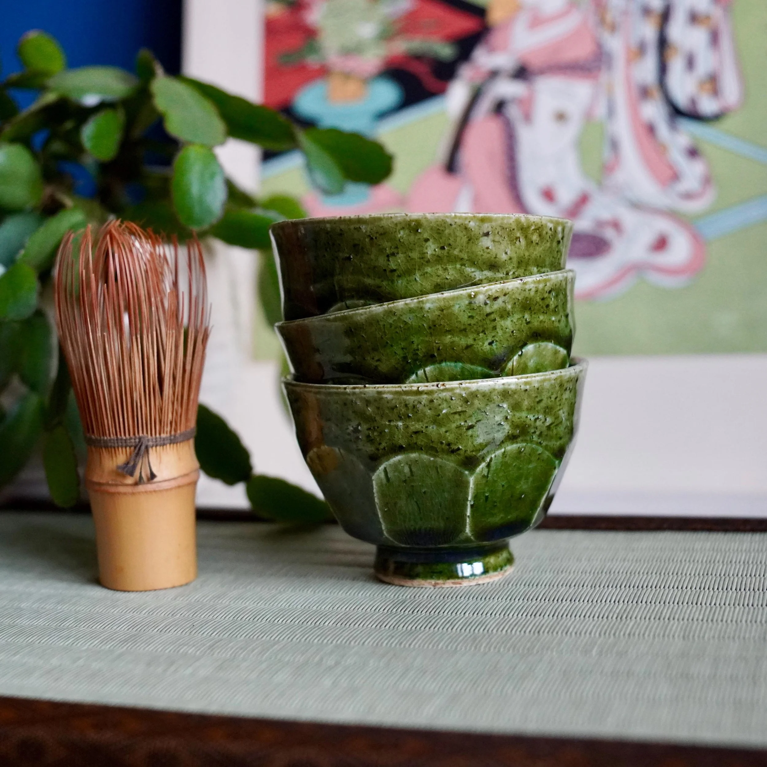 Faceted yunomi set of three oribe-yaki copper-green craquelé glaze Kyoto, late Shōwa period Japan, stacked, displayed next to chasen on tatami mat with ukiyoe print in background
