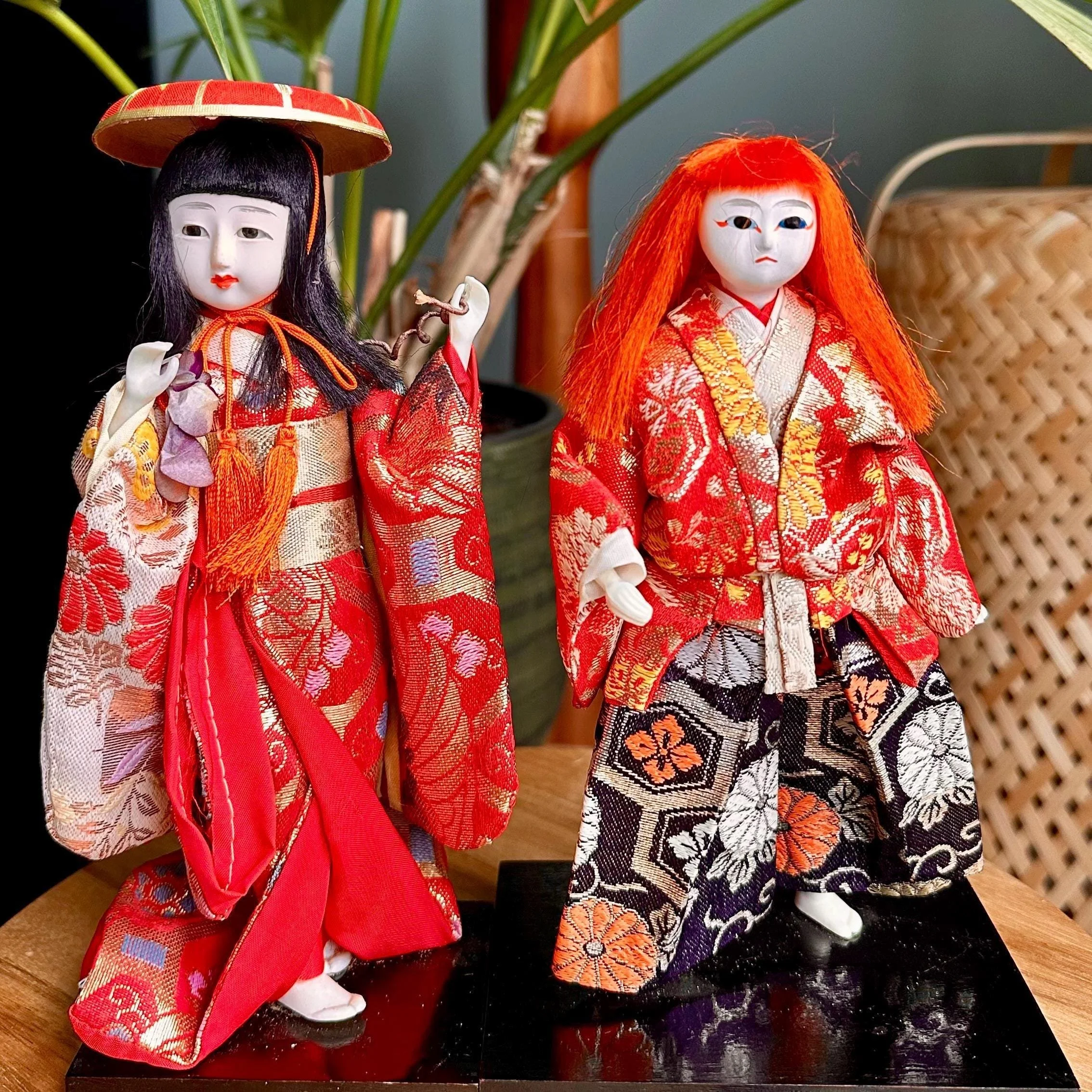 Kabuki ningyo doll pair: left doll in red kimono with black hair and hat; right doll in red and black, with wild orange hair and wider stance.