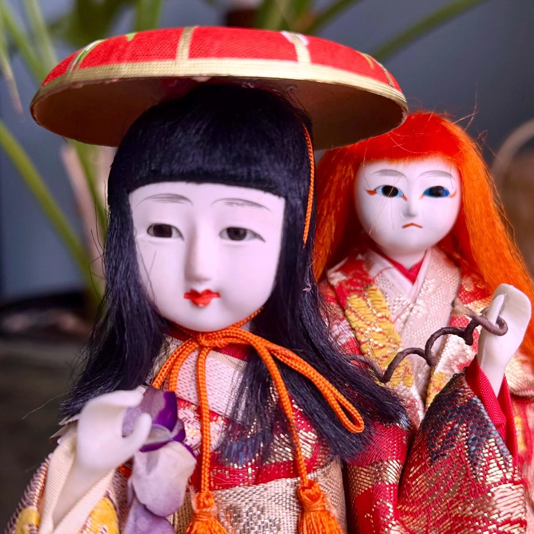 Pair of Kabuki ningyo dolls in red and gold kimonos. The black-haired doll wears a red hat; the orange-red haired doll has wild hair and holds a twisted branch.