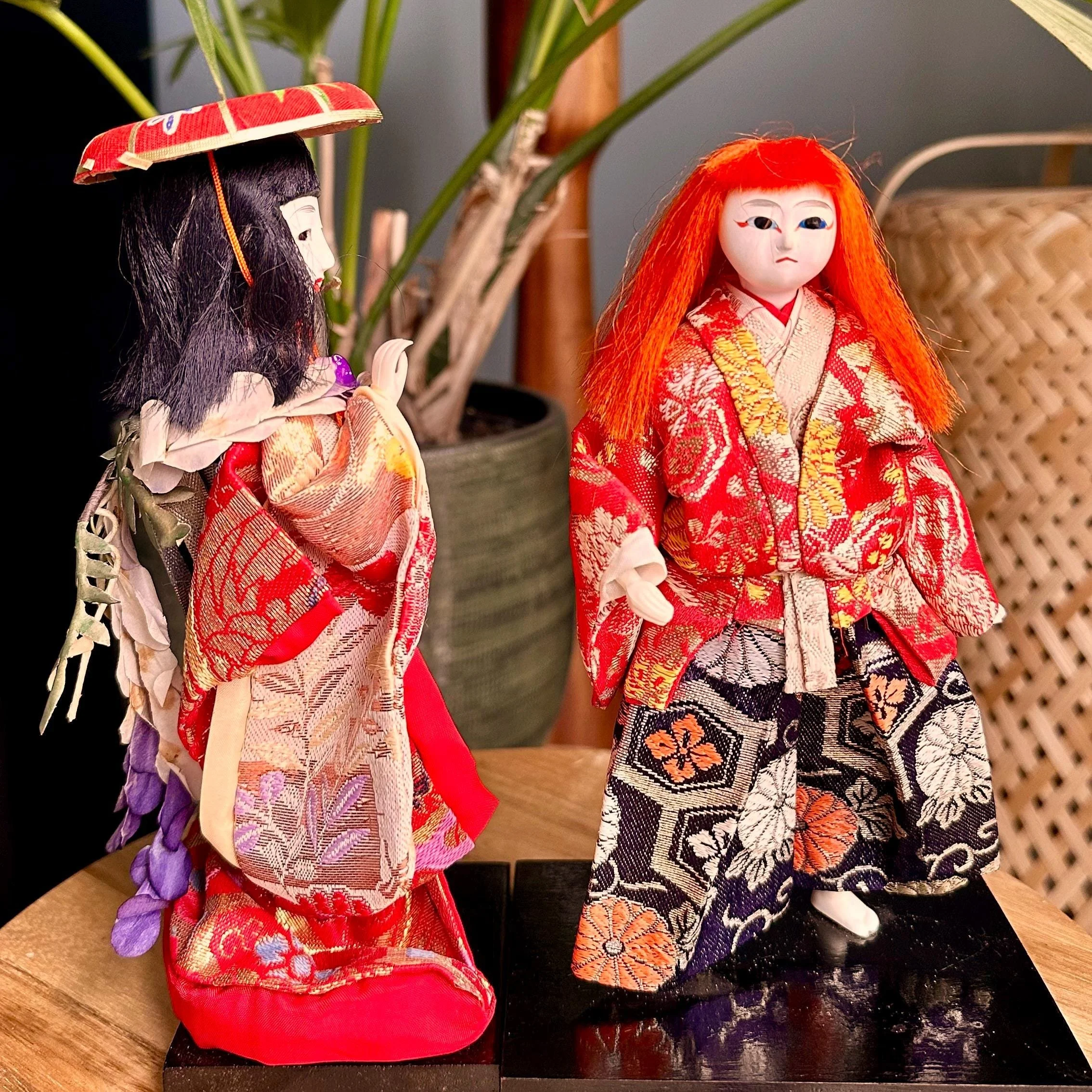 Kabuki ningyo dolls depicting Kagamijishi, one with black hair and a red hat, the other with wild red hair, both in elaborate red and gold kimonos on black stands.