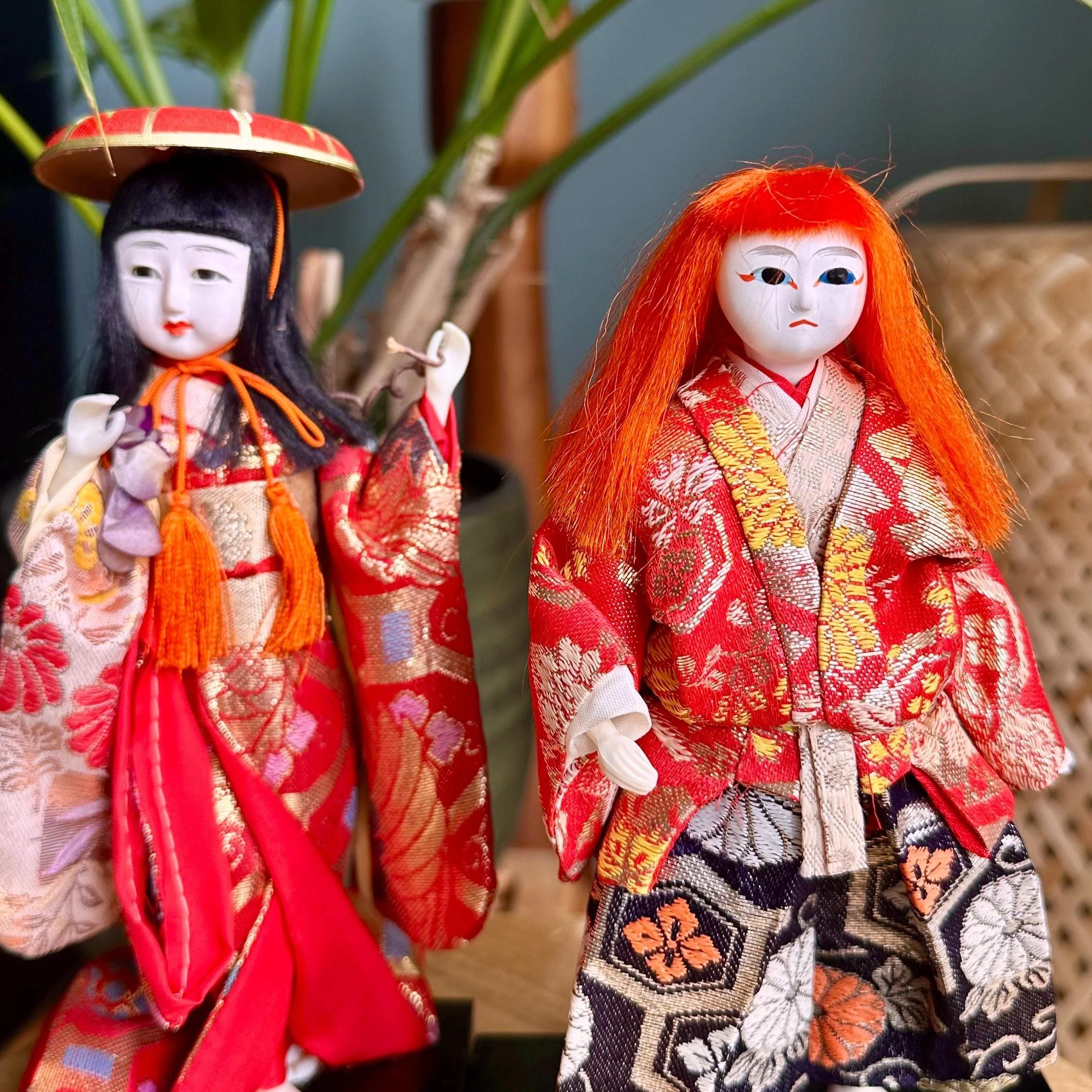Pair of Kabuki ningyo dolls. Left doll with black hair and red hat; right doll with wild orange-red hair. Both wear elaborate red, gold, and patterned silk kimonos.
