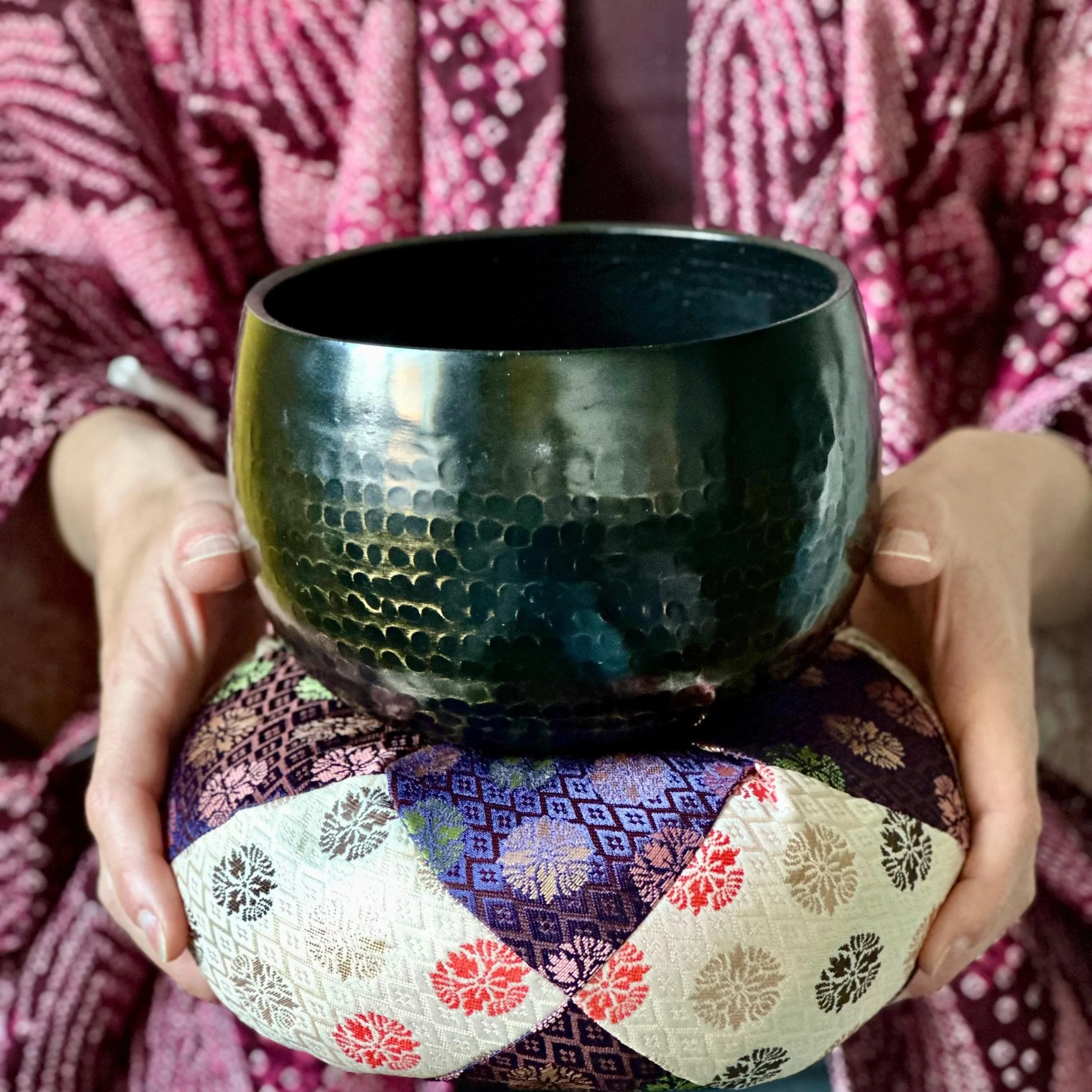 Vintage Japanese orin singing bowl hand-hammered tsuchime bronze with zabuton cushion and wooden striker, Shōwa period Japan, held in hands on pillow by woman wearing haori jacket