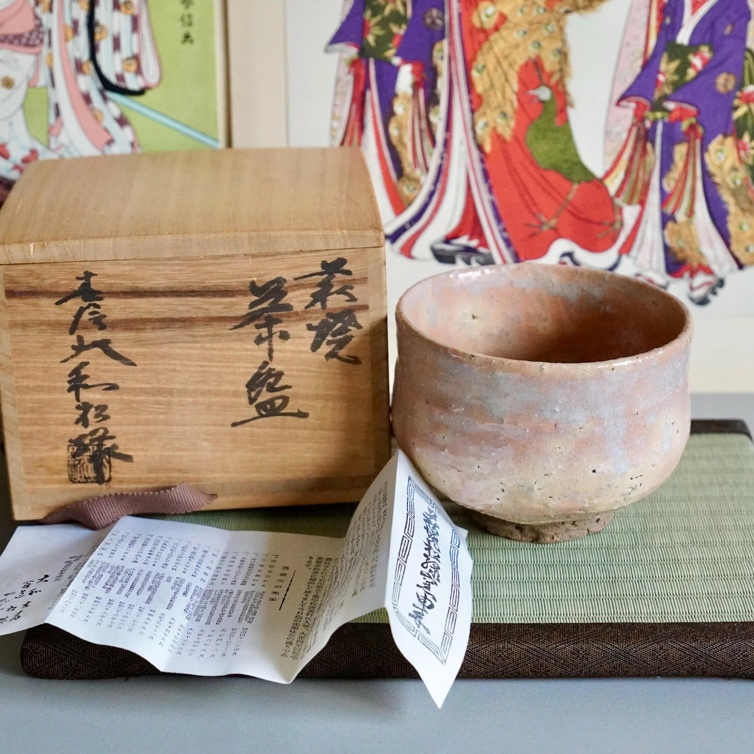 Hagi-yaki chawan Yamato Matsuroku-gama on wooden display stand, shira-Hagi glaze in warm peach tones, ukiyo-e prints in background