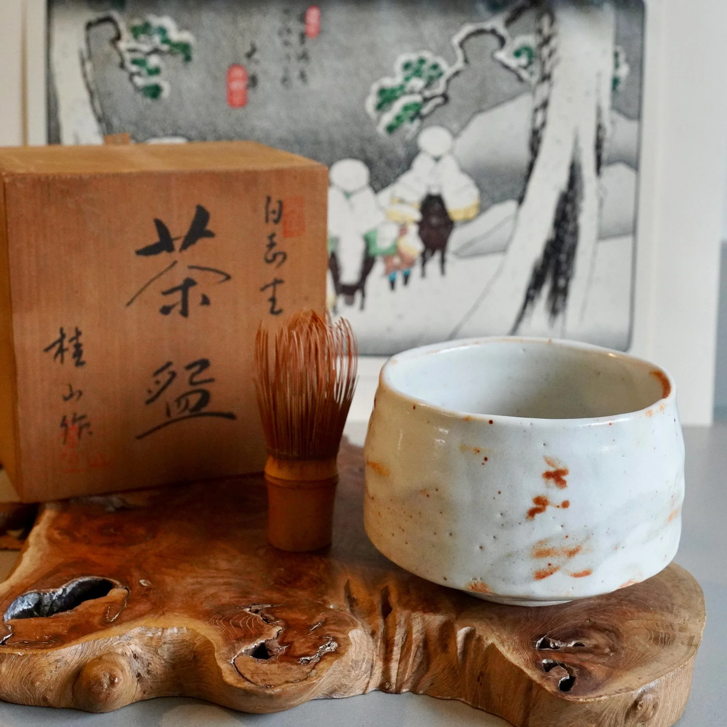 Shira-hagi chawan Taizan kiln white Hagi ware matcha bowl displayed on wooden plank with original tomobako, Shōwa period ca. 1960 to 1975 Japan, ukiyoe print in background