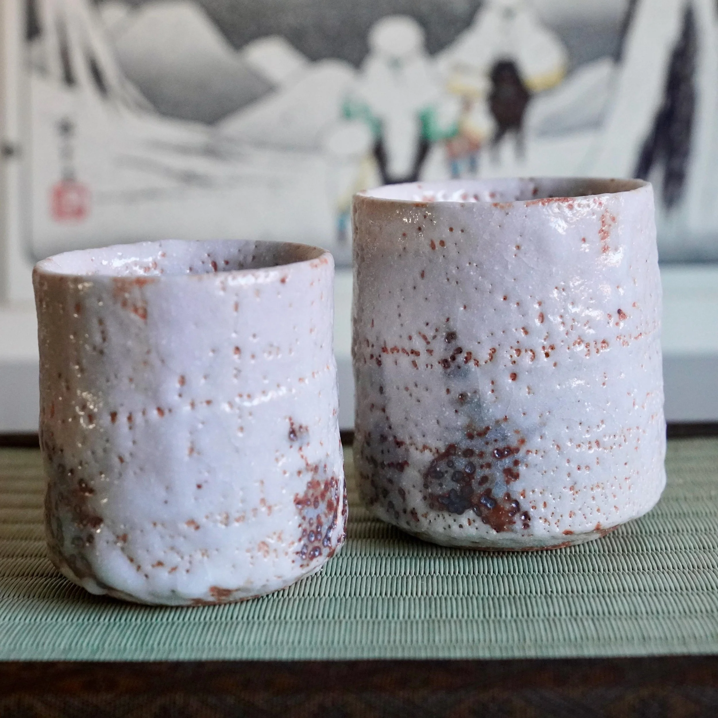 Two Shino yunomi by Katō Shōhei (Yōkun), featuring a textured white glaze with reddish-brown and dark iron spots, on a tatami mat.