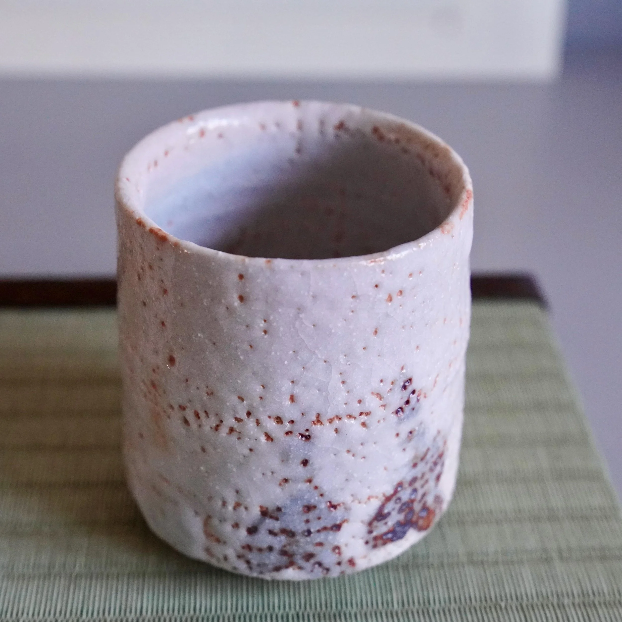 Shino yunomi by Katō Shōhei (Yōkun), an off-white cup featuring a rough, speckled surface with reddish-brown iron spots.