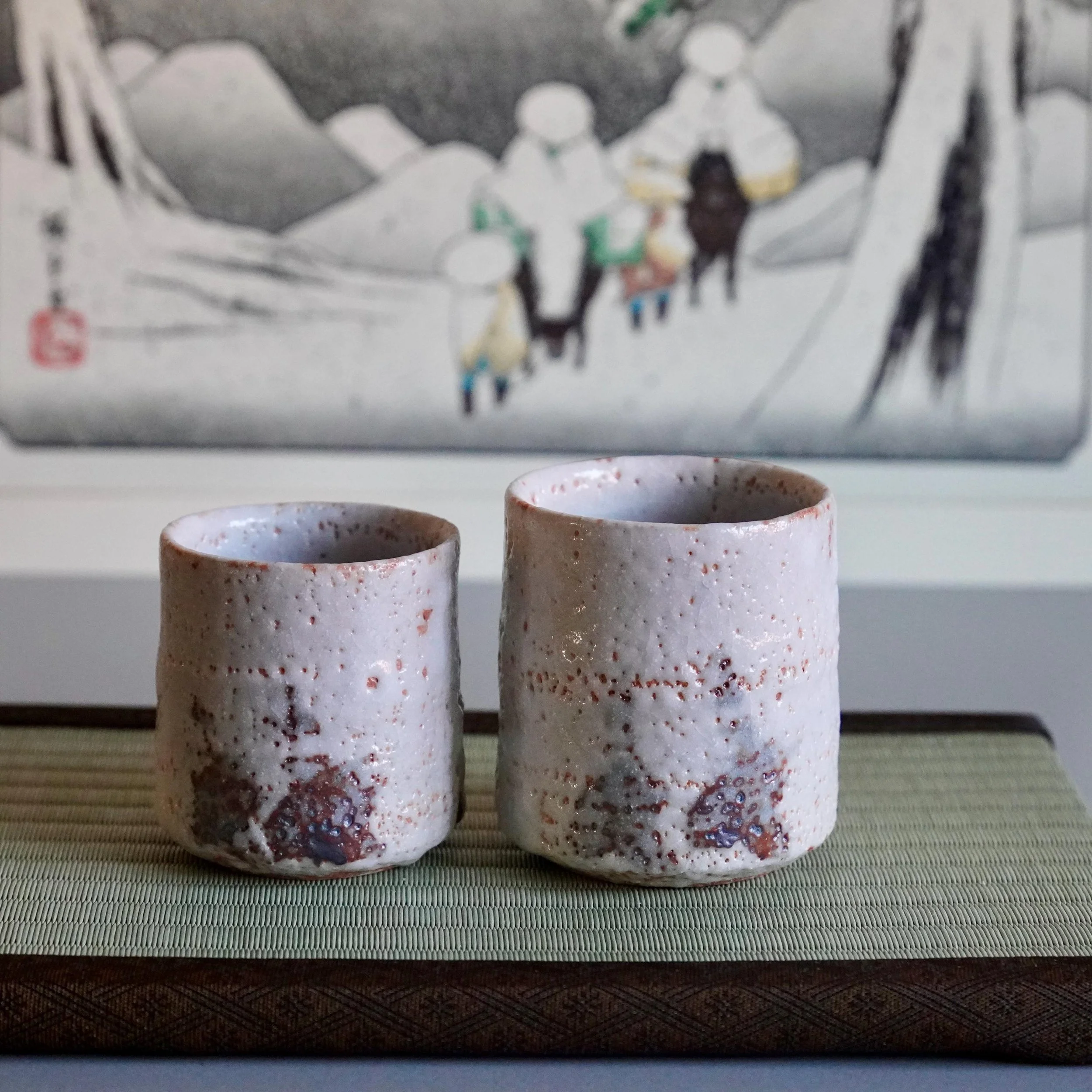 Katō Shōhei (Yōkun) Shino yunomi. Two cups of different sizes with thick, rough off-white glaze, reddish-brown accents, and dark speckles.