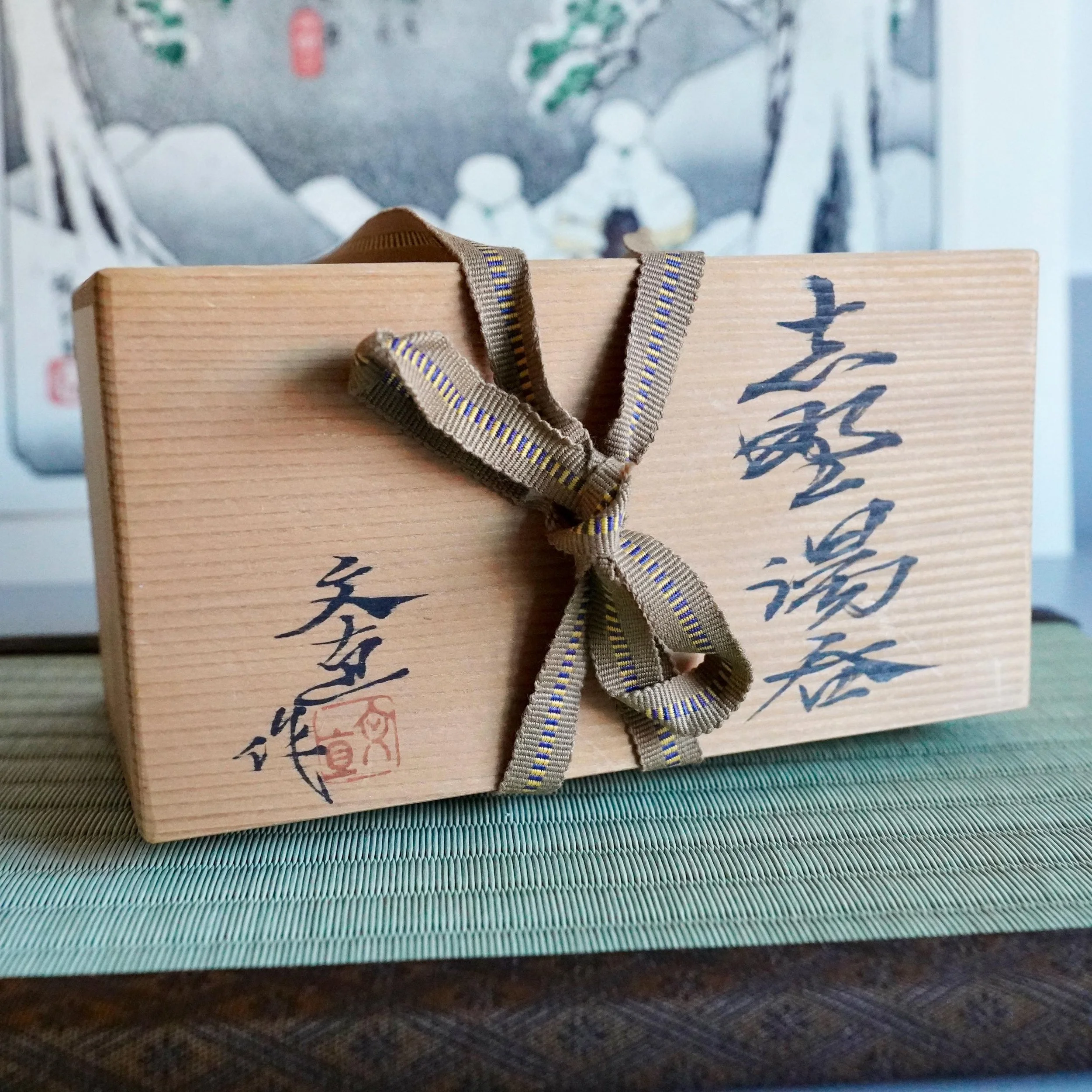 Katō Shōhei (Yōkun) wooden tomobako, tied with a khaki ribbon featuring yellow and blue zigzag, inscribed with black calligraphy and a red seal.