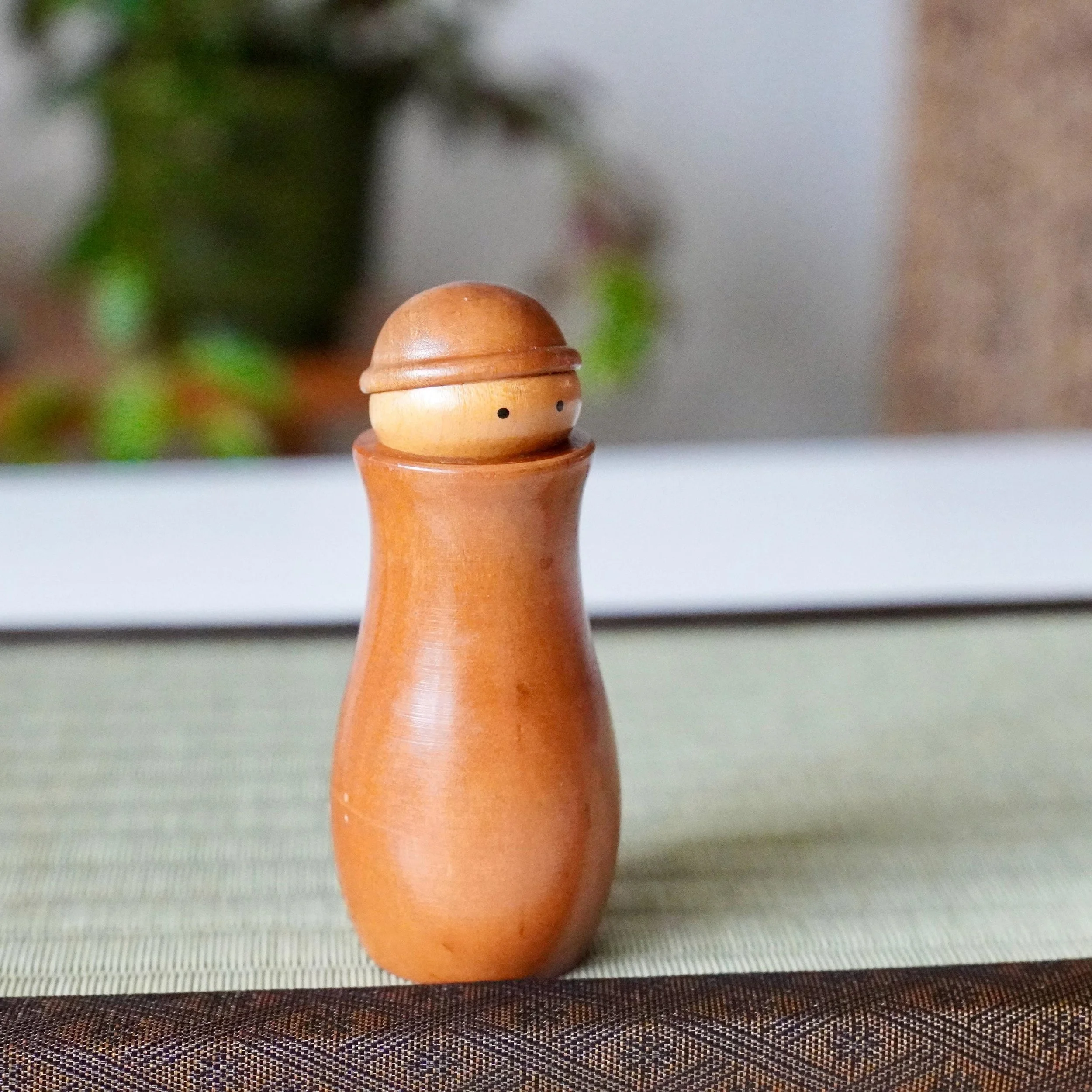 Kōkyū minimalist wooden kokeshi toothpick holder with simple dot eyes, front view on a tatami mat.