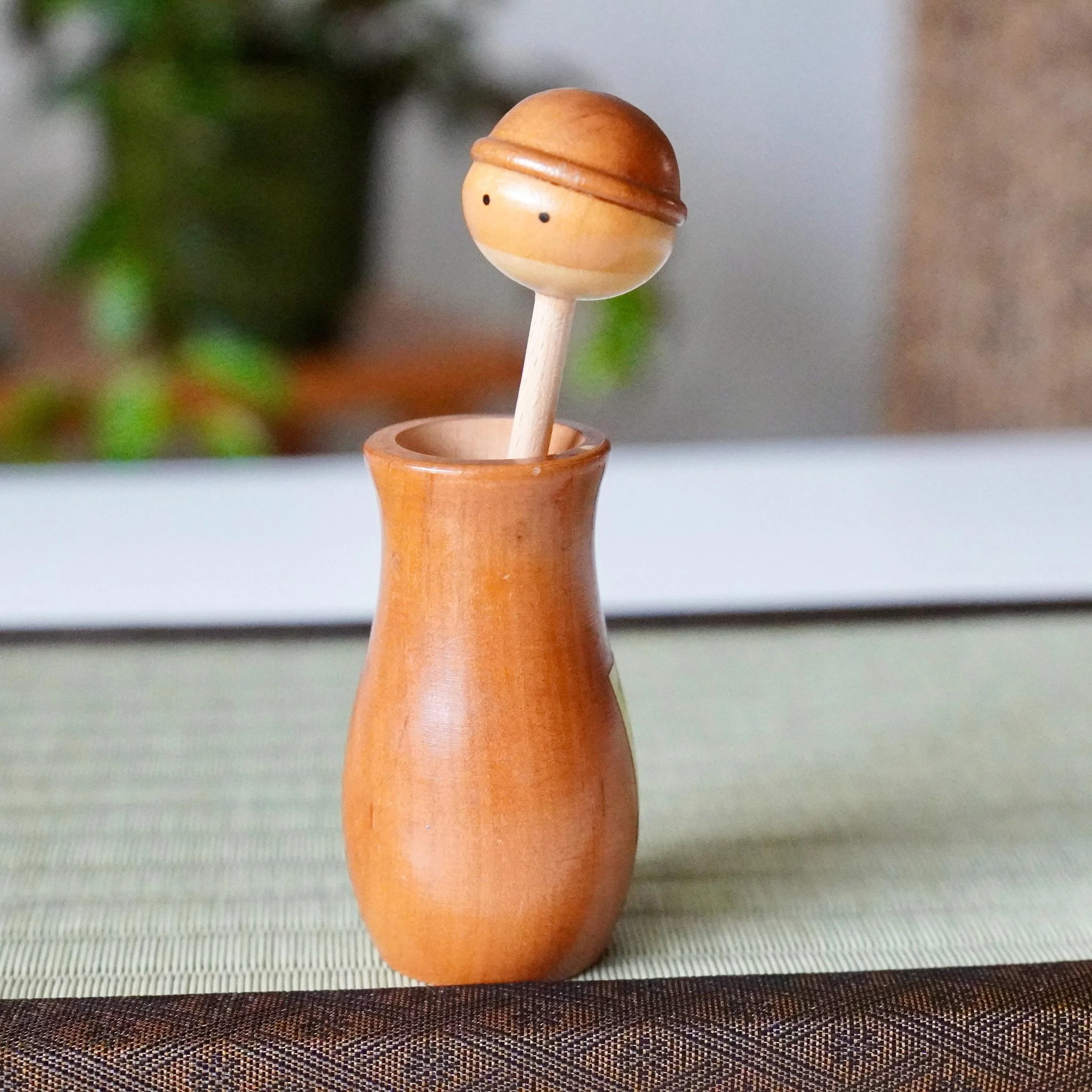 Kōkyū minimalist wooden kokeshi toothpick holder, with a round head, simple eyes, and smooth light brown finish, on a tatami mat.