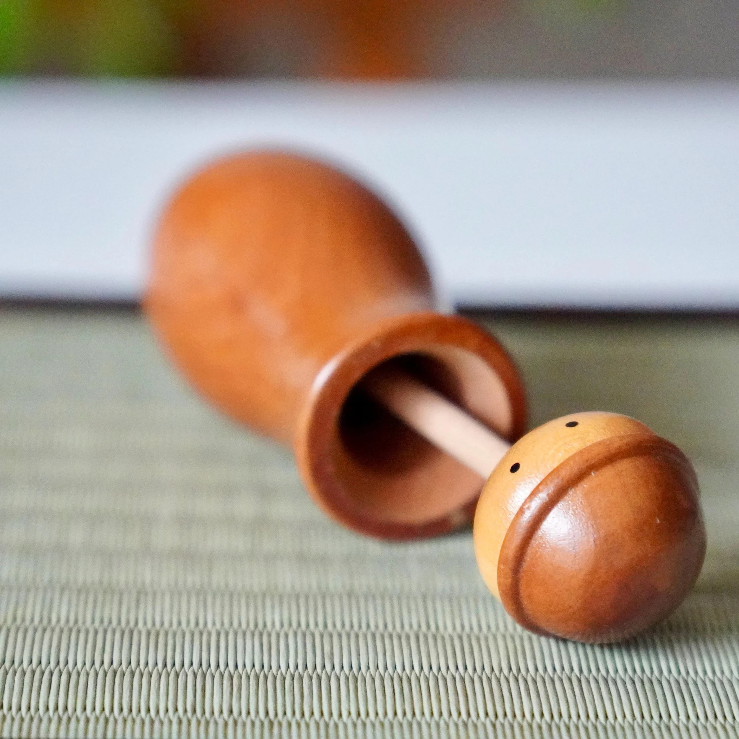 Kōkyū wooden kokeshi toothpick holder, smooth light brown, on a tatami mat. Head separated to reveal a hollow stem, an inner stick, and two black dots.