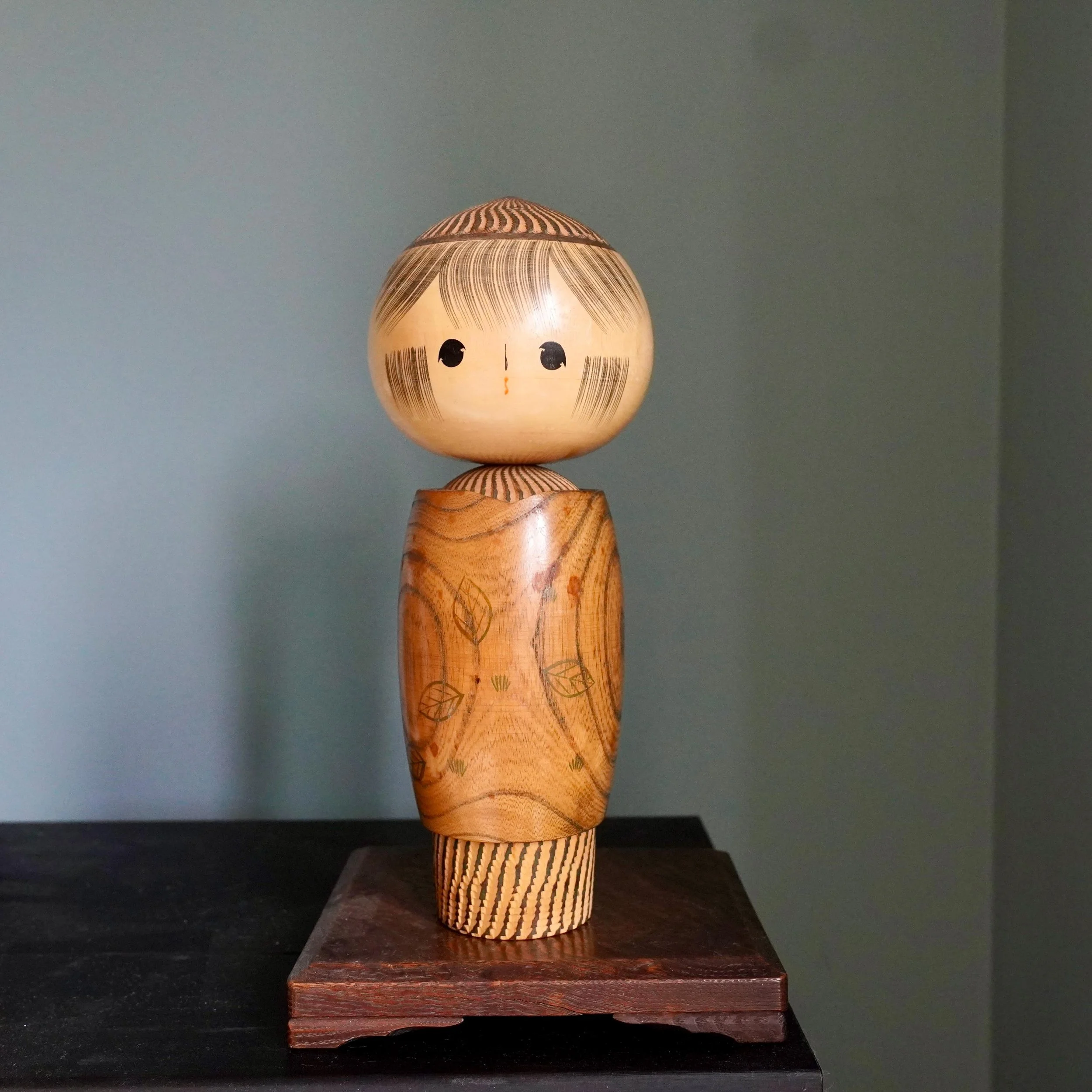 Large sōsaku kokeshi Tamura Noboru 28cm keyaki natural grain body with leaf motifs and burnt stripe decoration, displayed on wooden stand,Shōwa period Japan