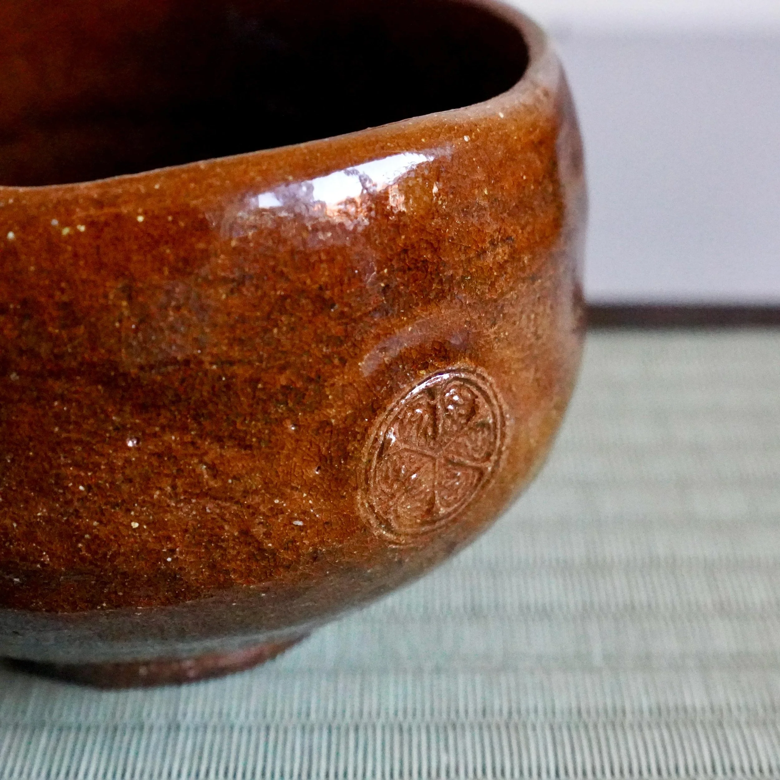 Ōbi-yaki chawan side view with ame-yu caramel glaze and floral stamp