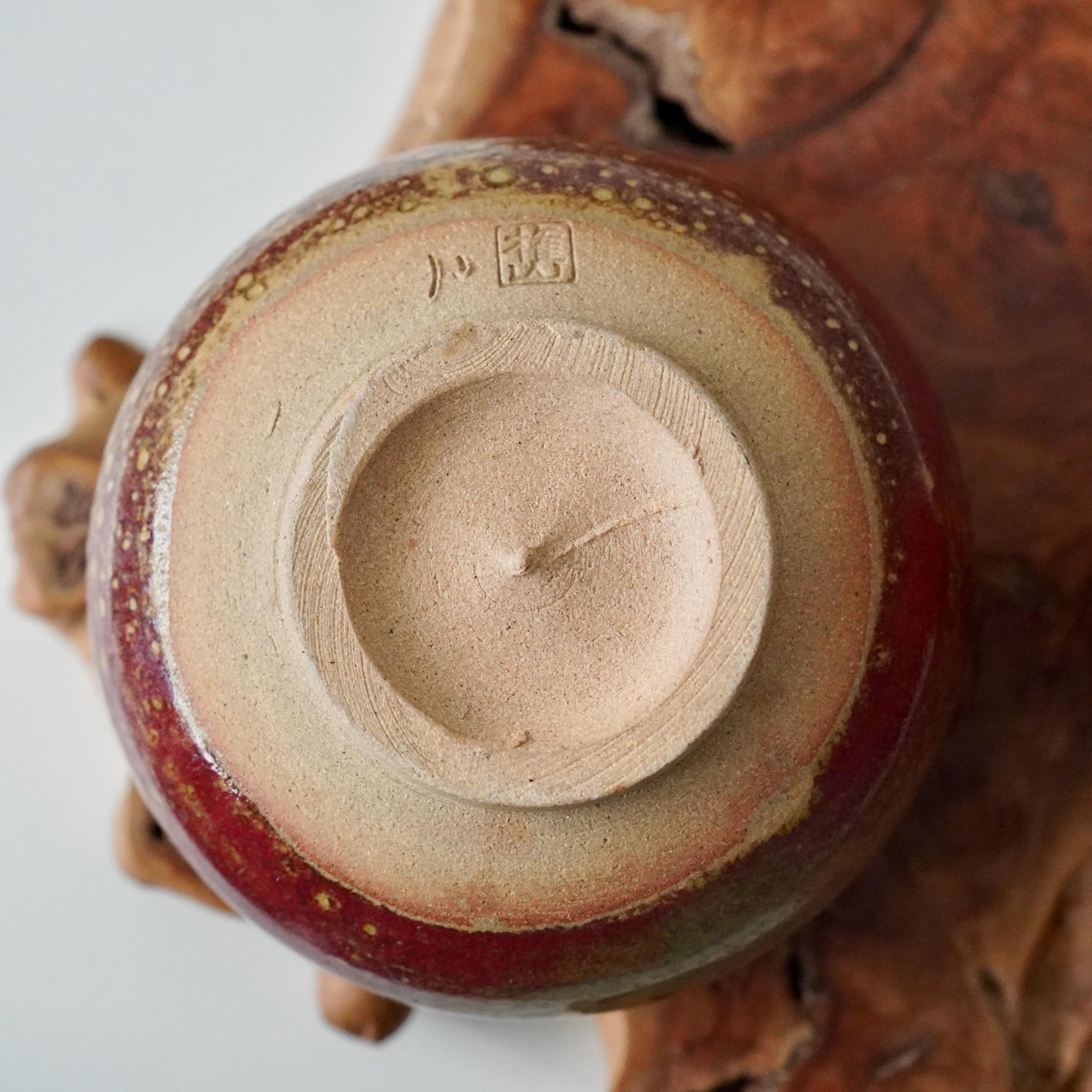 Kenzan's Yōhen glazed chawan underside, with an unglazed sandy base featuring horizontal striations and the 権山 signature near the deep red, speckled glazed rim.