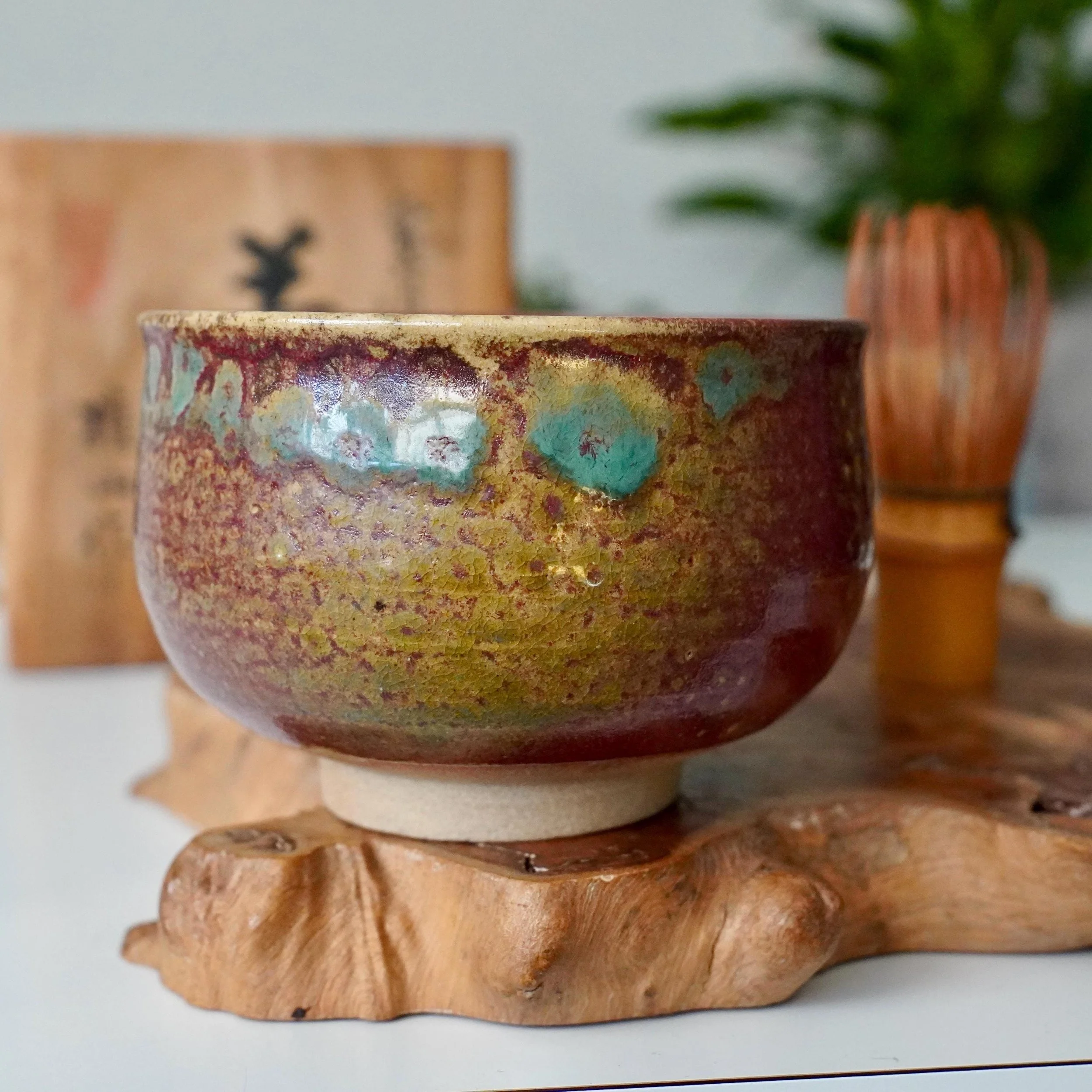 Kenzan's Tokoname-yaki chawan with yōhen glaze, featuring rich ruby, gold, and turquoise colors on a crackled surface, on a carved wooden stand.