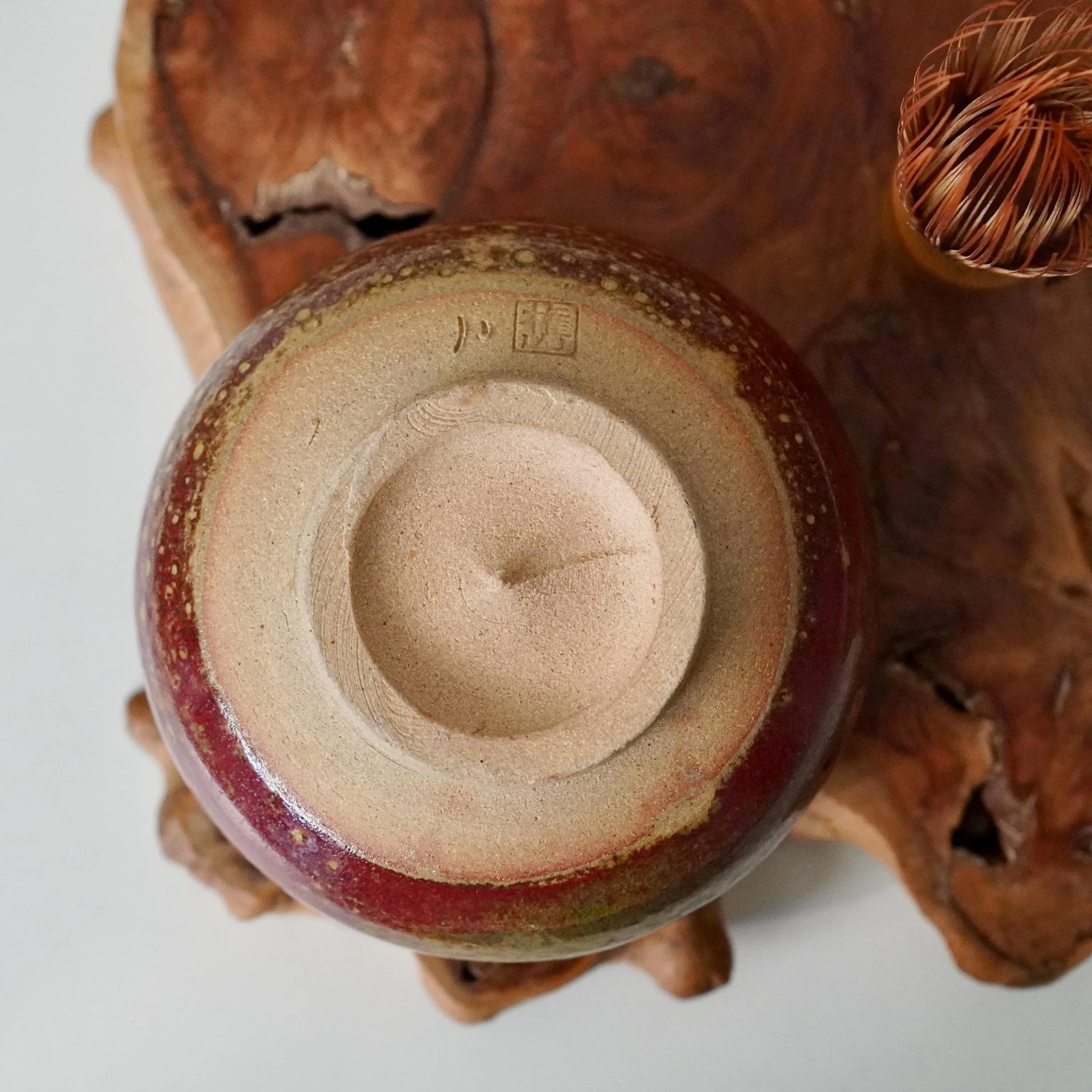 Underside of a red-glazed chawan, showing its unglazed tan footring and a square potter's mark with Japanese characters, Kenzan (権山).