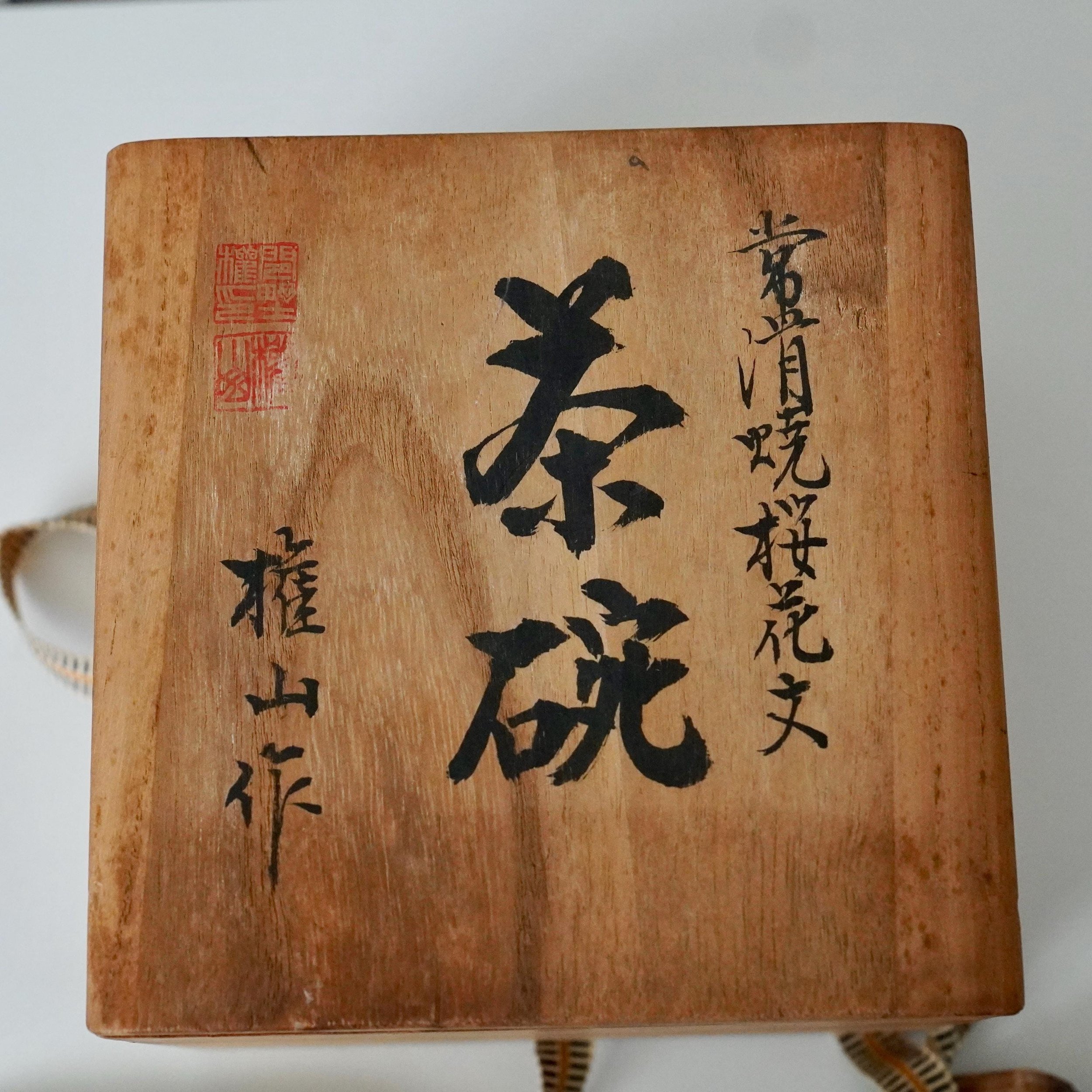 Light wooden tomobako lid with black calligraphy detailing a Yōhen cherry blossom tea bowl, signed by Kenzan, and a red seal.