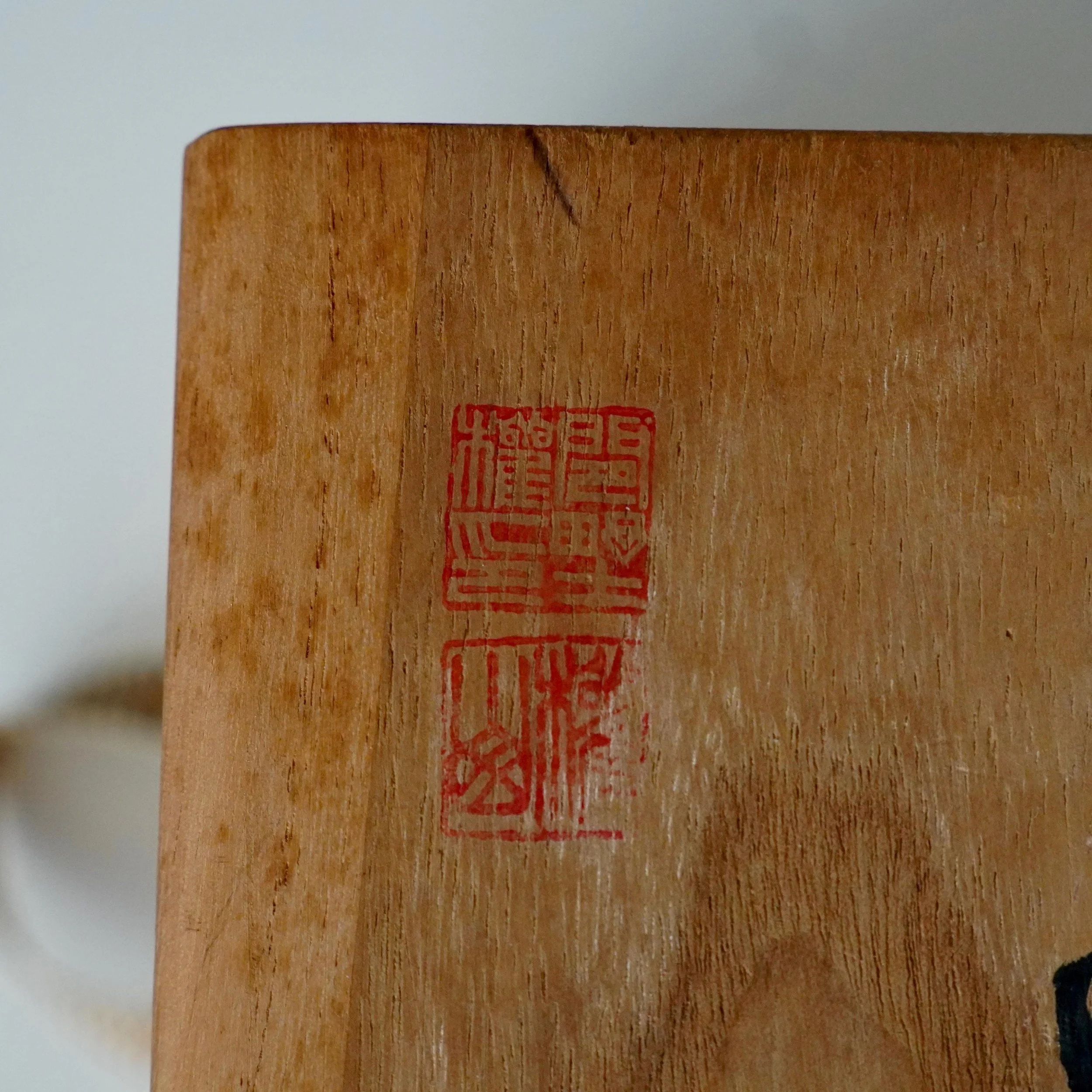 Close-up of a light brown wooden tomobako lid, showing vertical grain and two stacked red ink seals. The upper seal is Kenzan's signature.