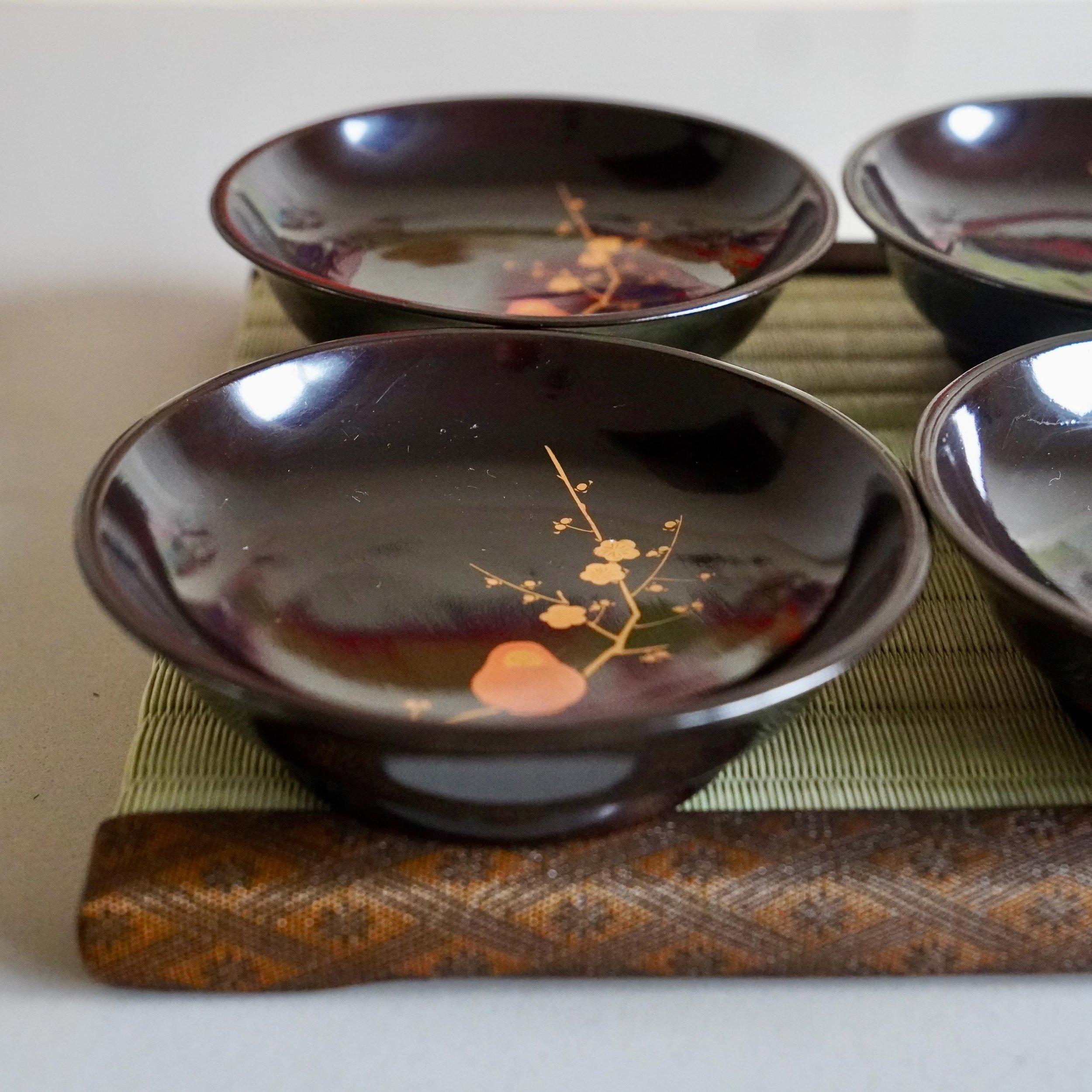 Four black urushi lacquer plates stacked on bamboo tatami mat