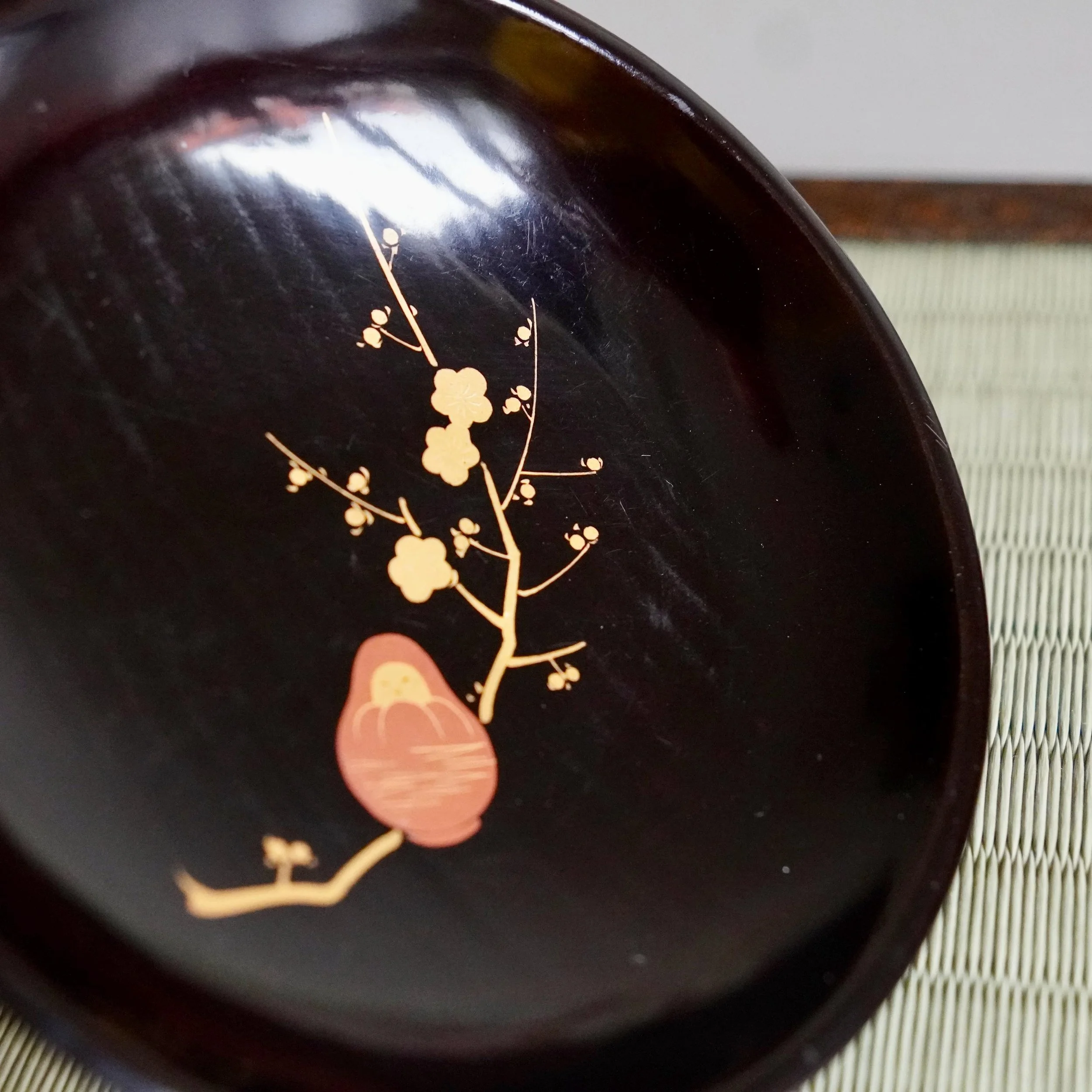 Detail of gold and coral maki-e Daruma design on lacquer plate rim
