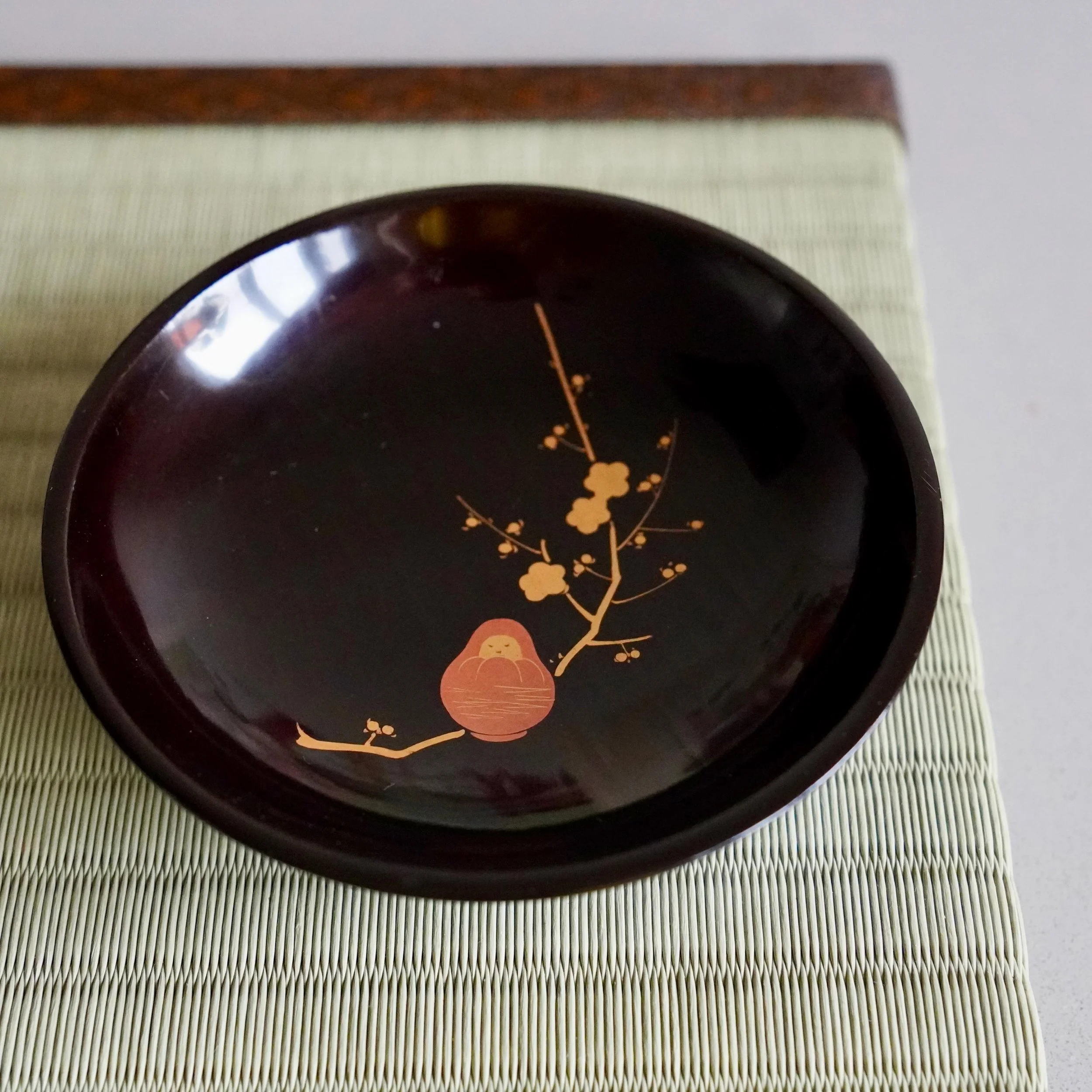 Black lacquer tea ceremony plate with maki-e plum and Daruma, overhead view