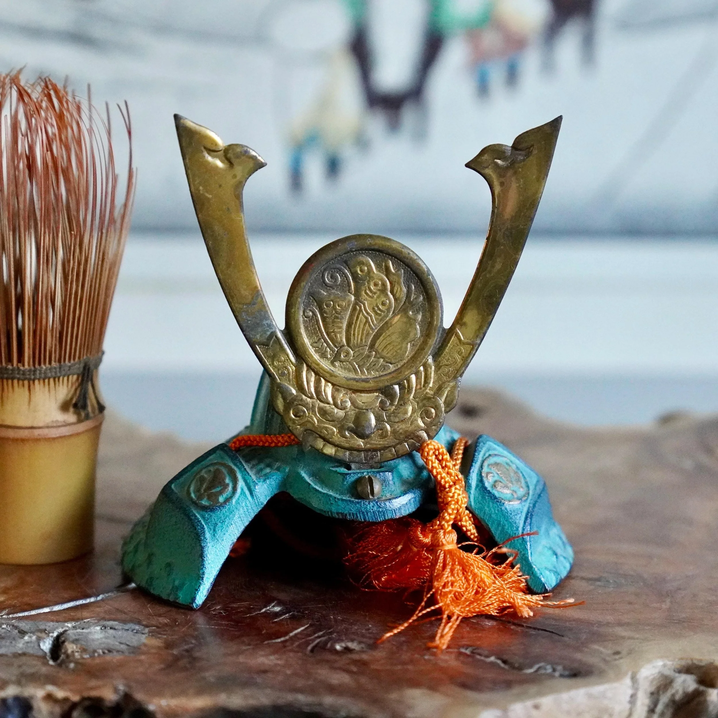 Nanbu Tekki cast iron kabuto samurai helmet with phoenix medallion aged green and gold patina next to chasen whisk for size on wooden plank Shōwa period Japan