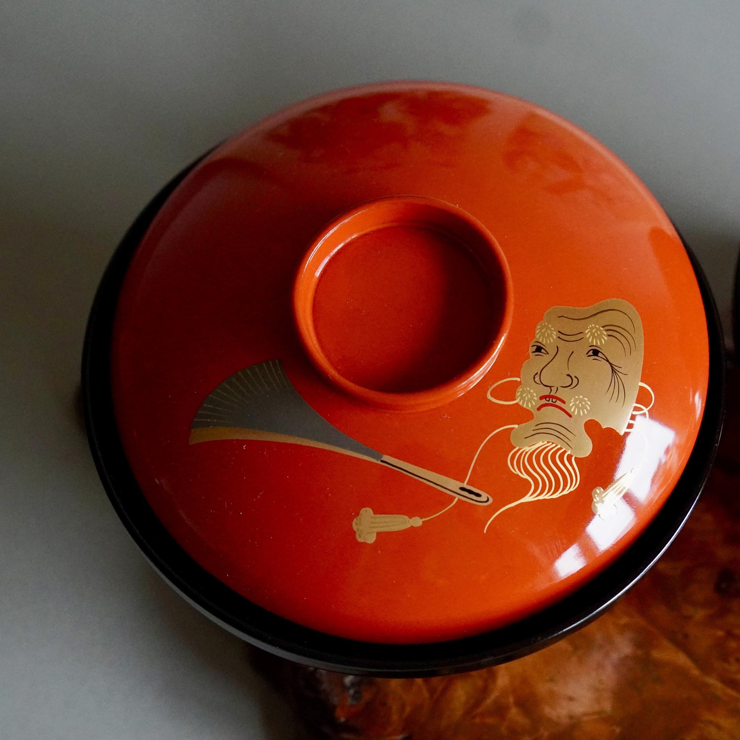 Overhead view of vermillion lacquer owan lid with gold Okina mask motif