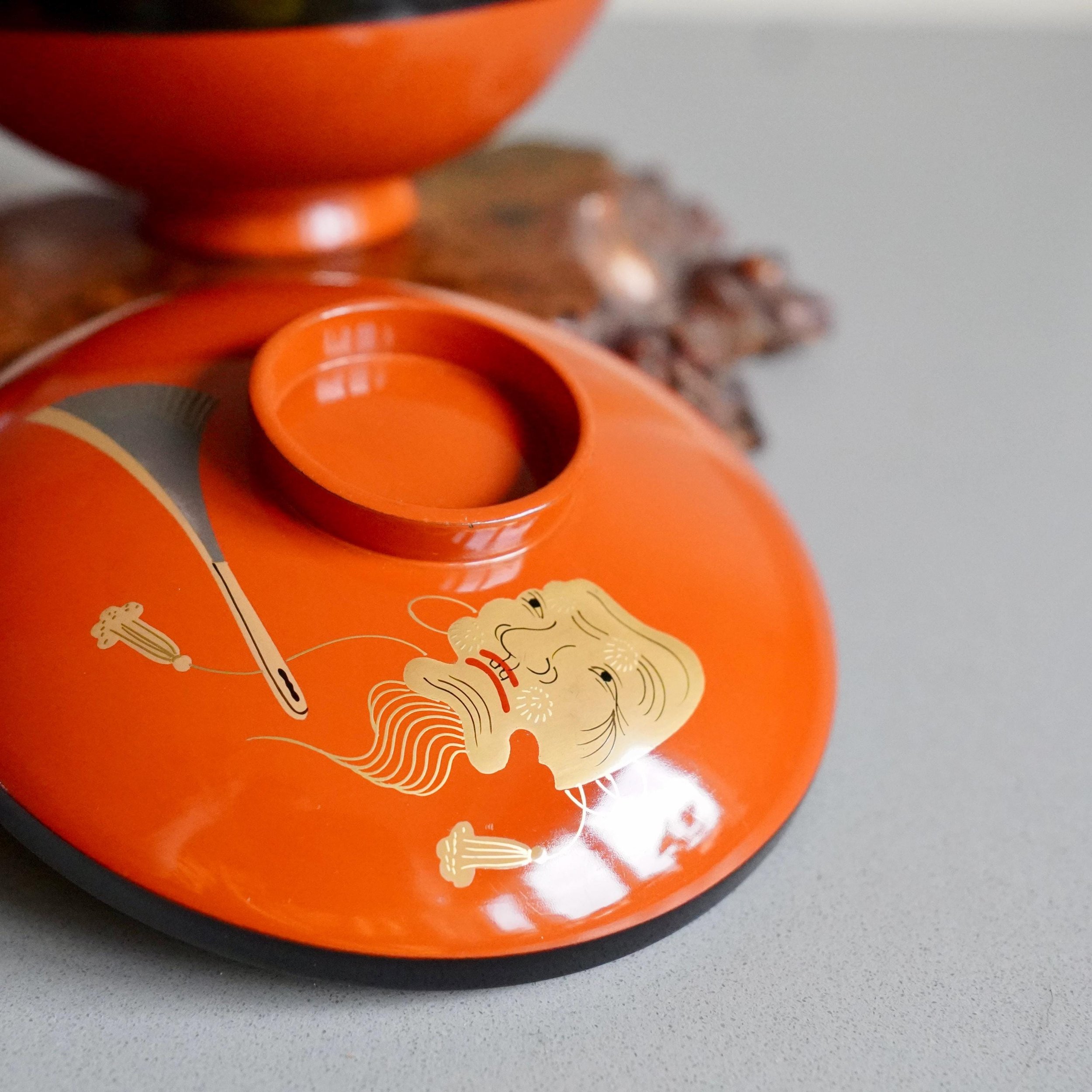 Close up of gold maki-e Okina mask design on urushi lacquer lid