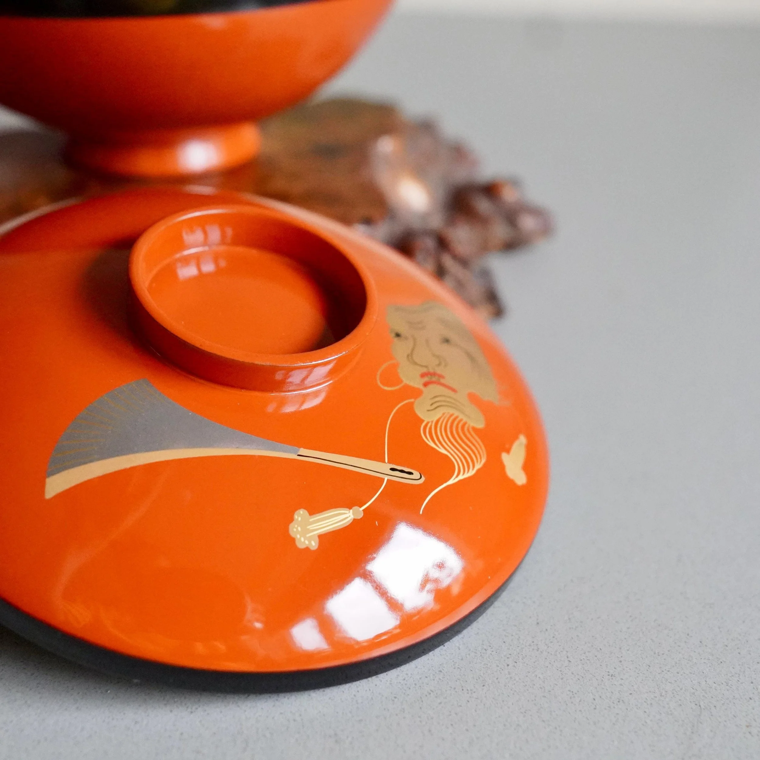 Vermillion urushi lacquer owan lid with gold Okina mask, angled view