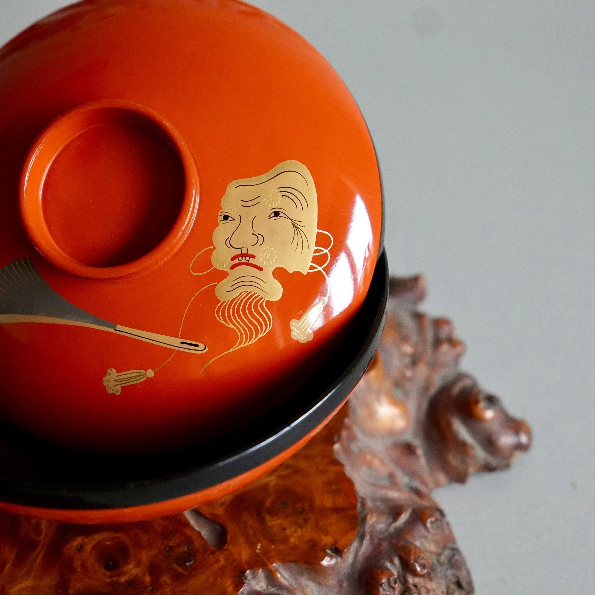 Vermillion lacquer owan lid with gold Okina mask, close side view